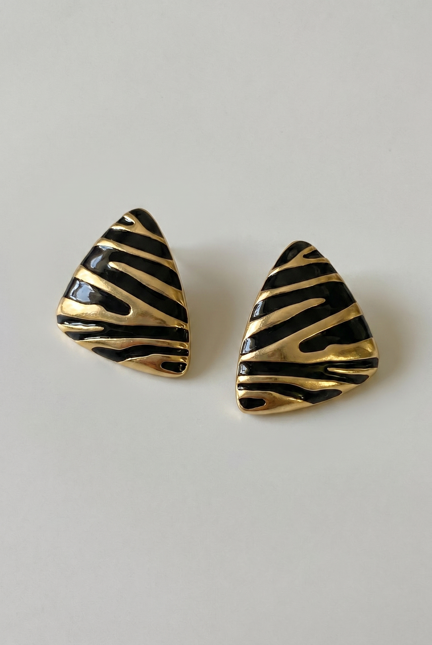 Pair of gold and black striped earrings on a light gray background