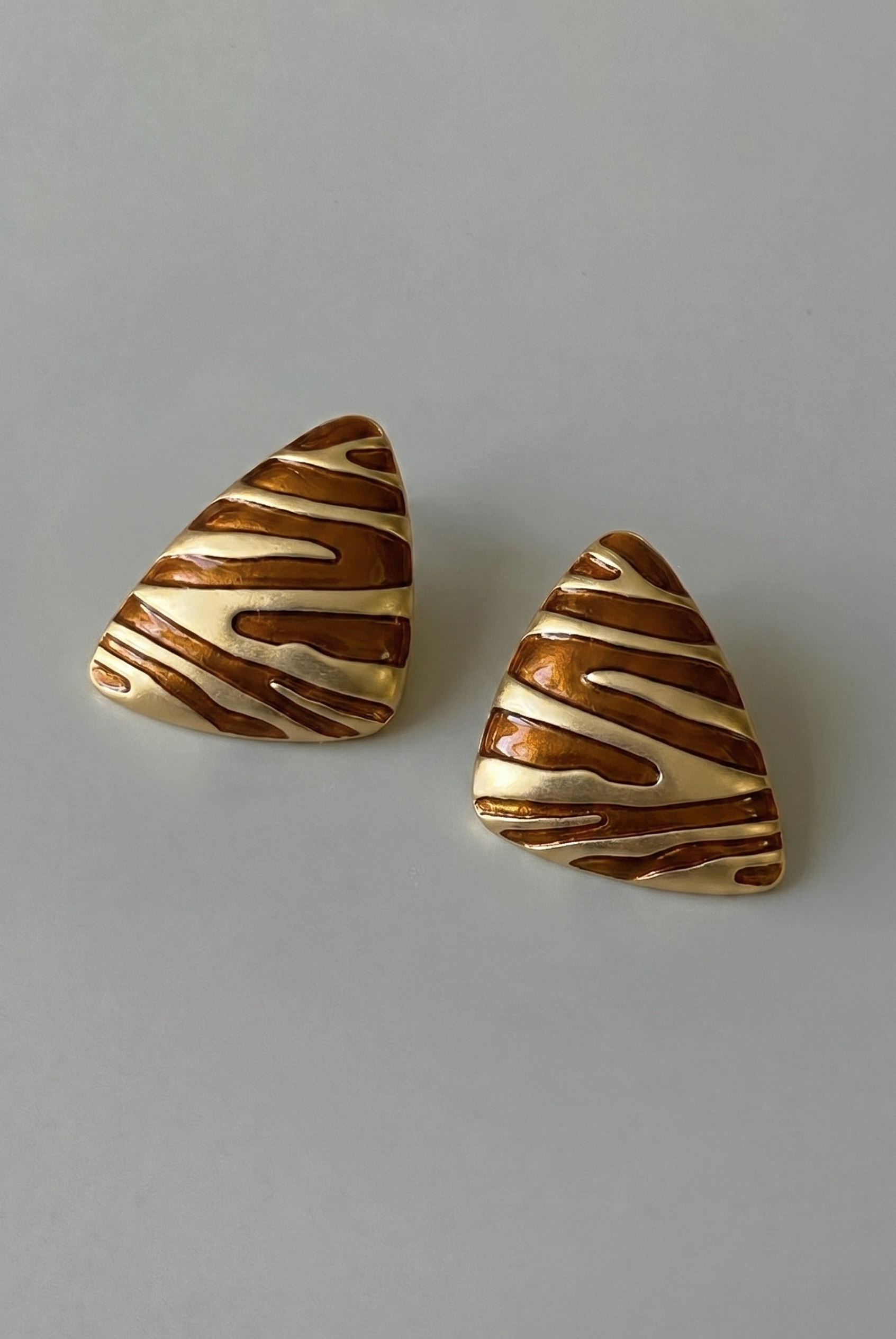 Pair of triangular earrings with striped pattern on a gray background