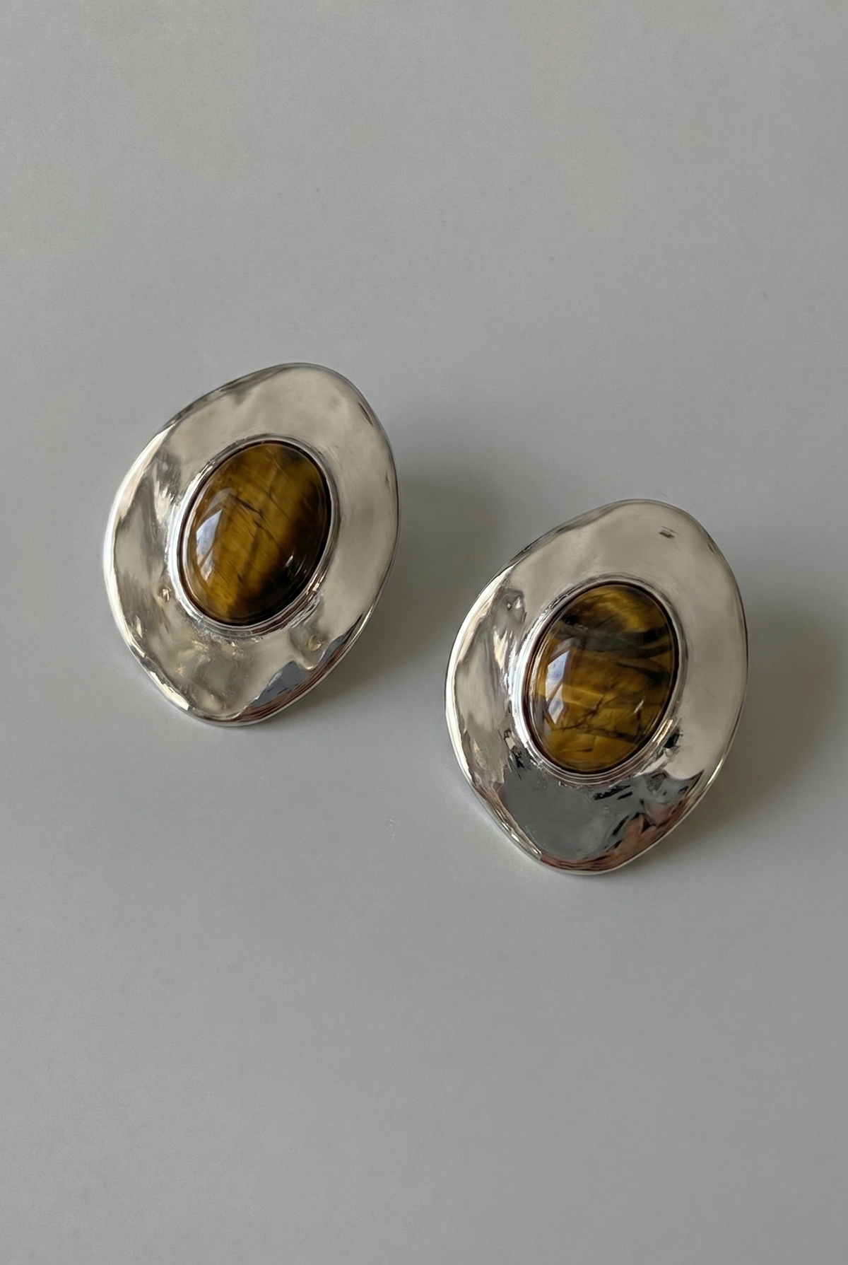 Pair of silver earrings with tiger's eye stones on a gray background
