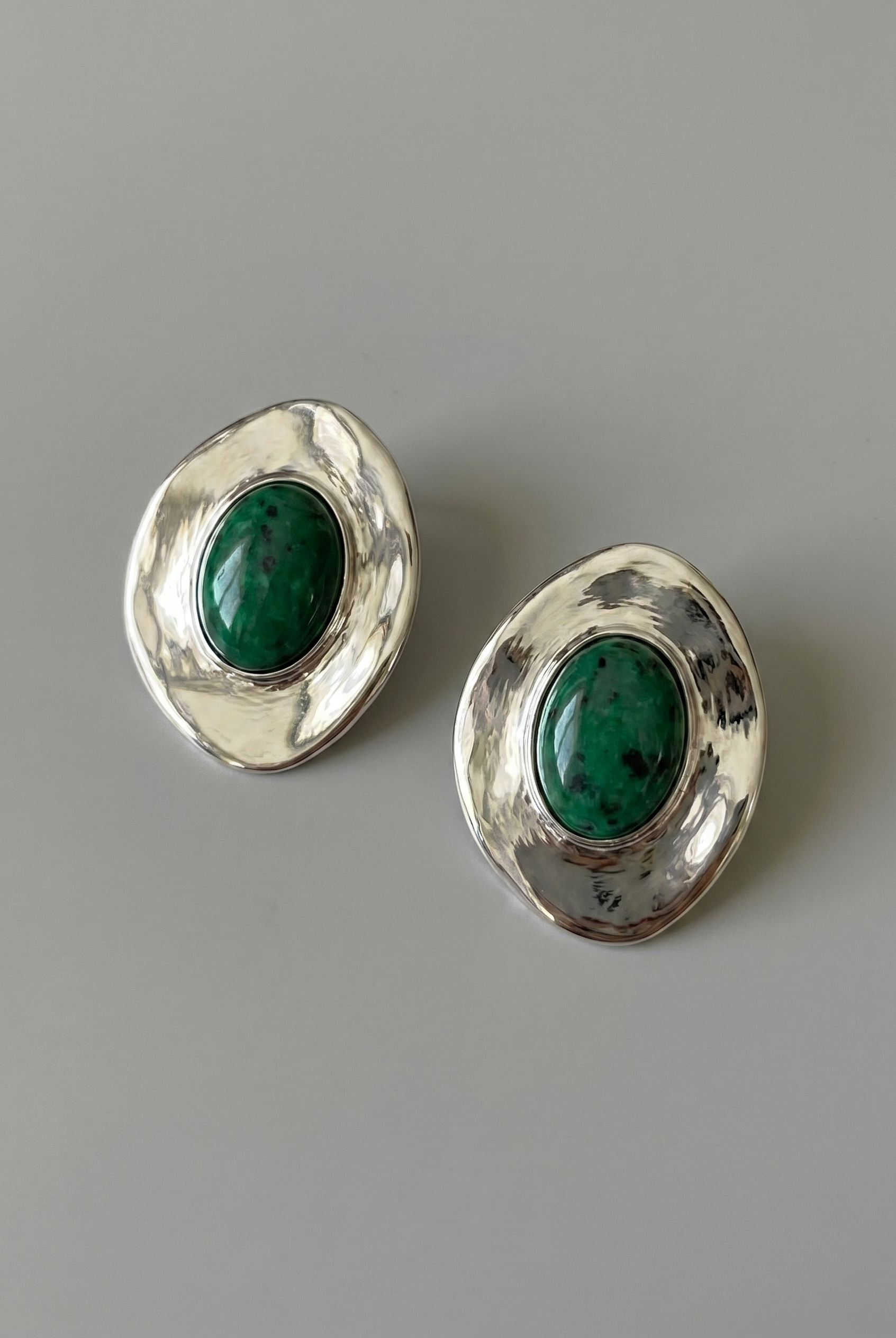 Pair of silver earrings with green gemstones on a gray background