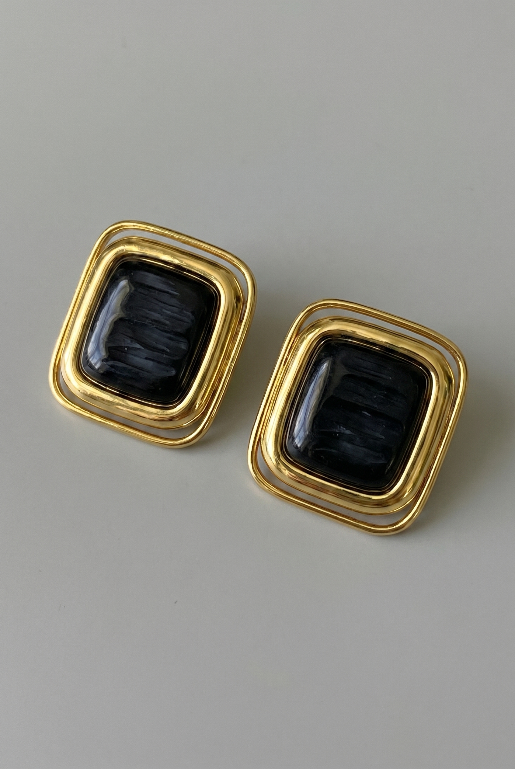 Pair of gold earrings with black stones on a gray background