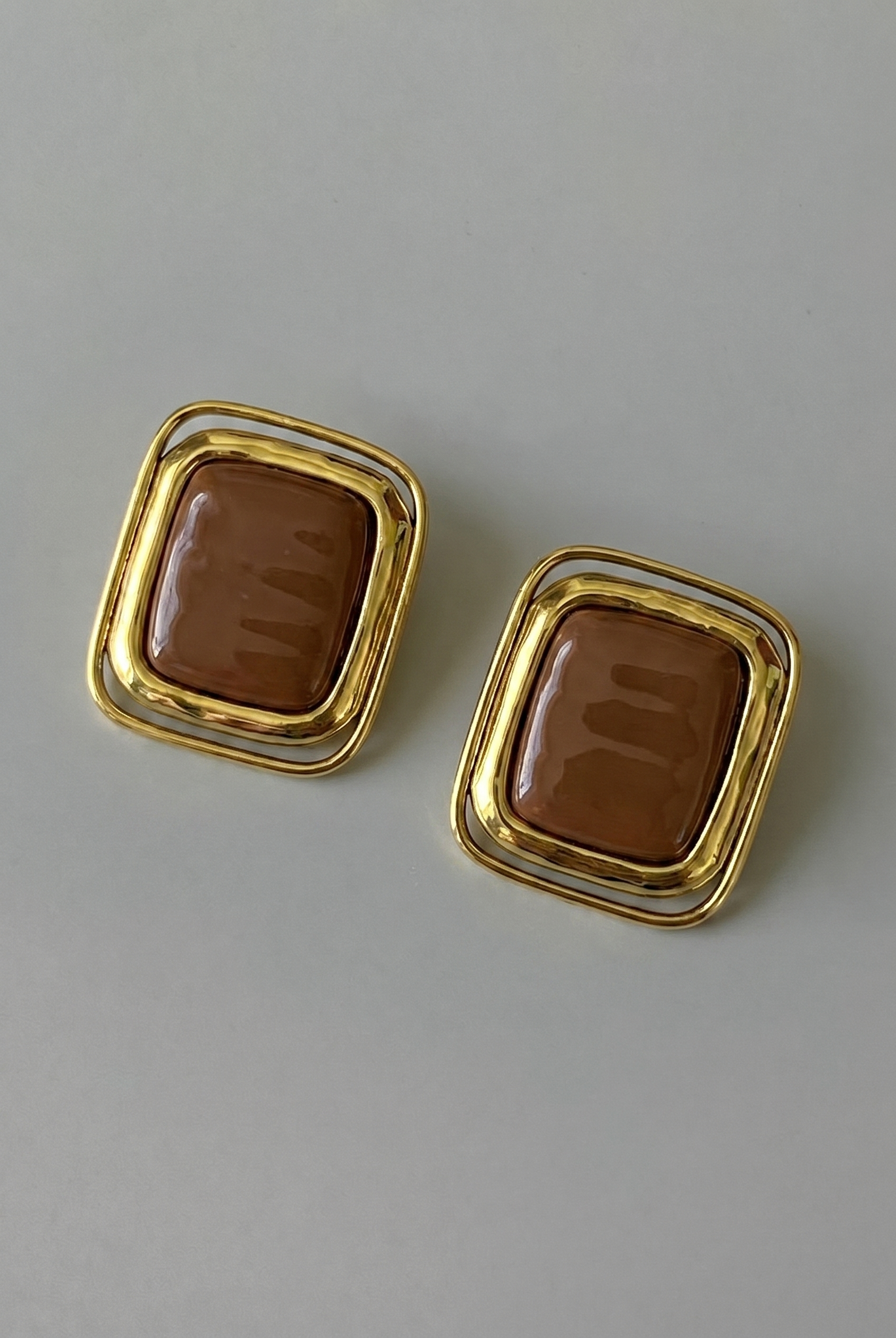 Pair of gold-framed brown square earrings on a light gray background