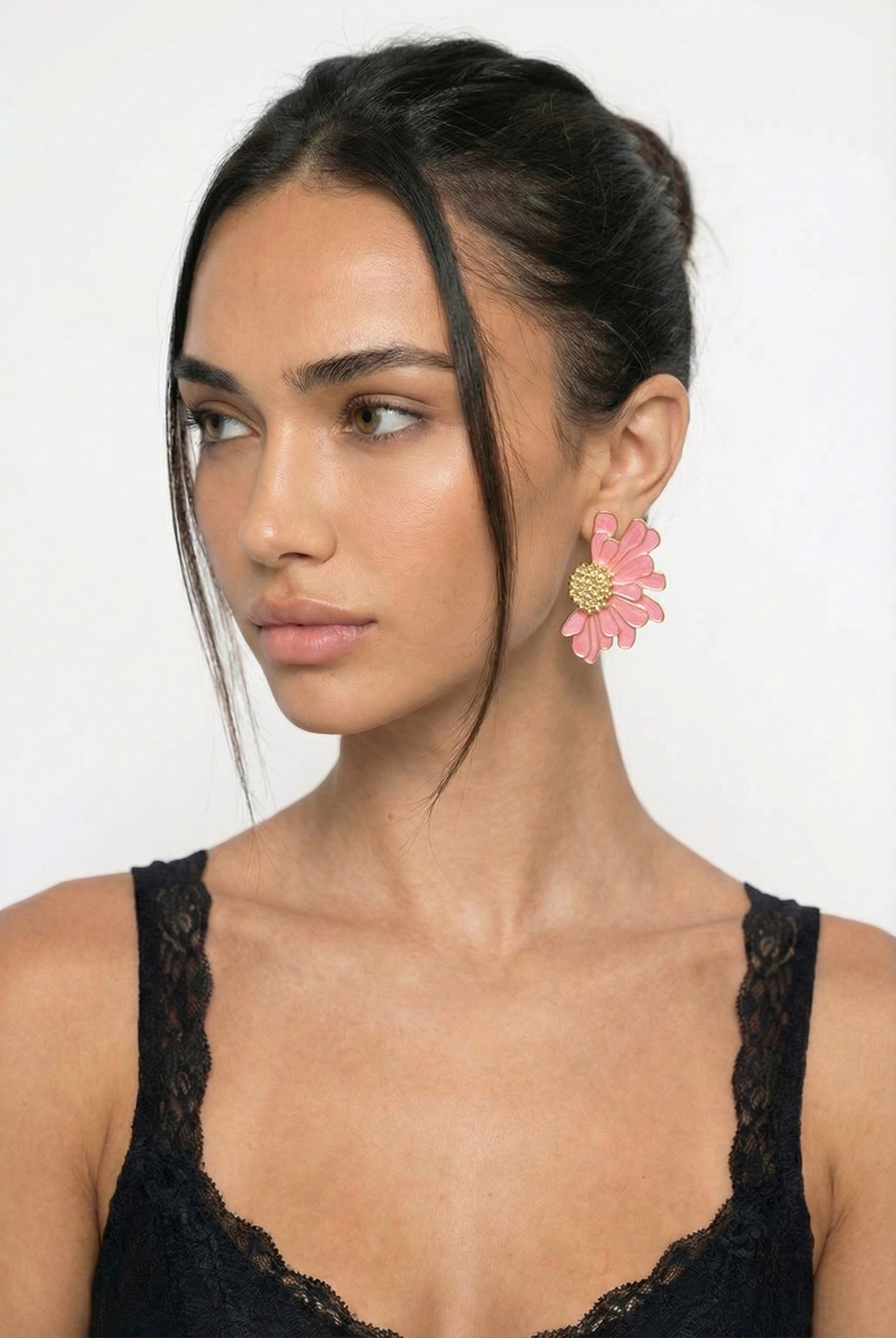 Woman wearing a black lace top with pink floral earrings against a white background