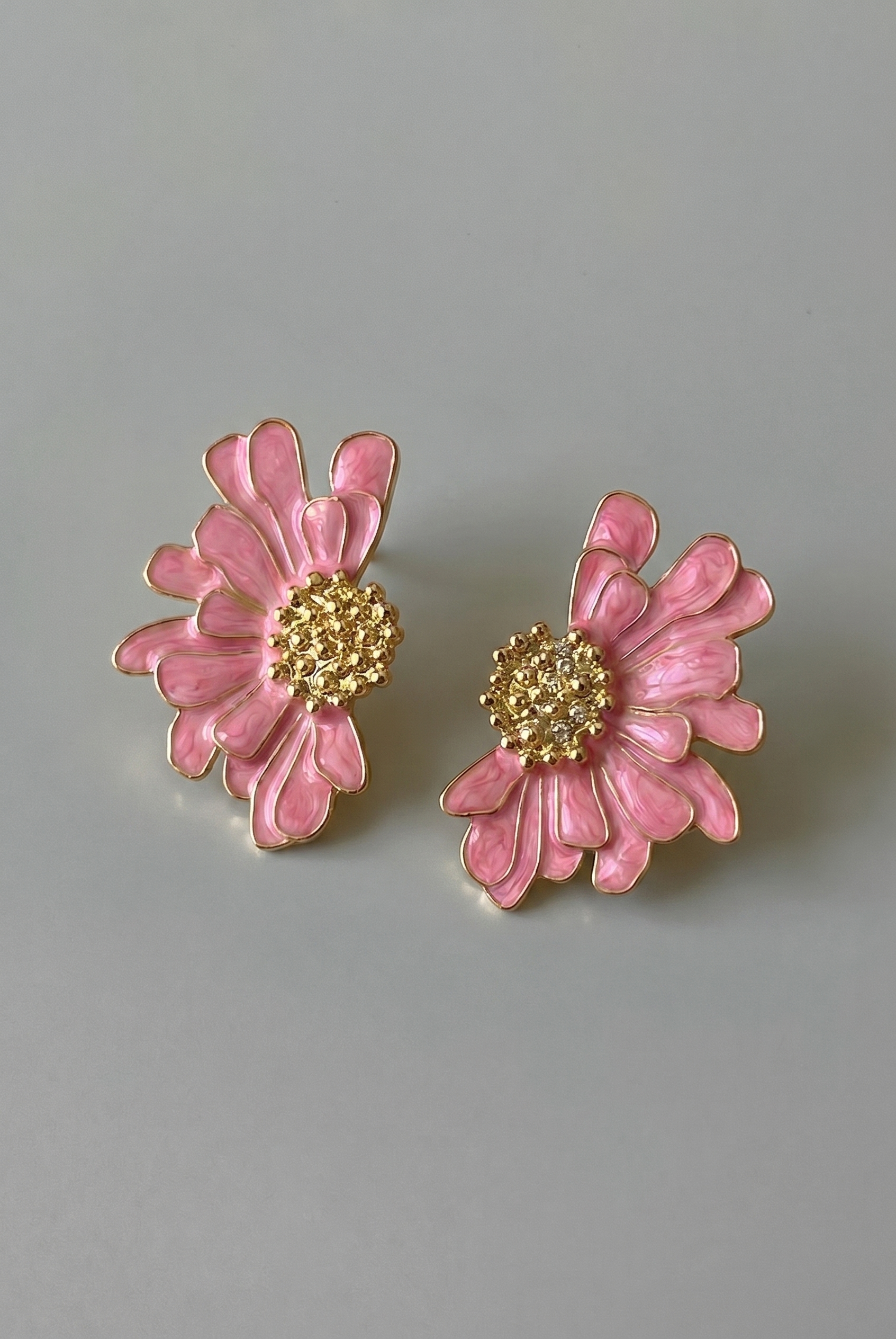 Pink flower-shaped earrings with gold centers on a gray background