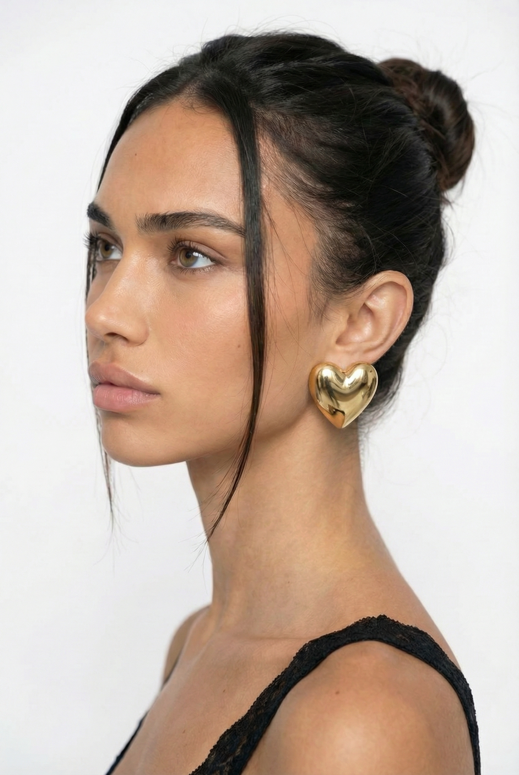 Woman wearing gold heart-shaped earrings on a white background