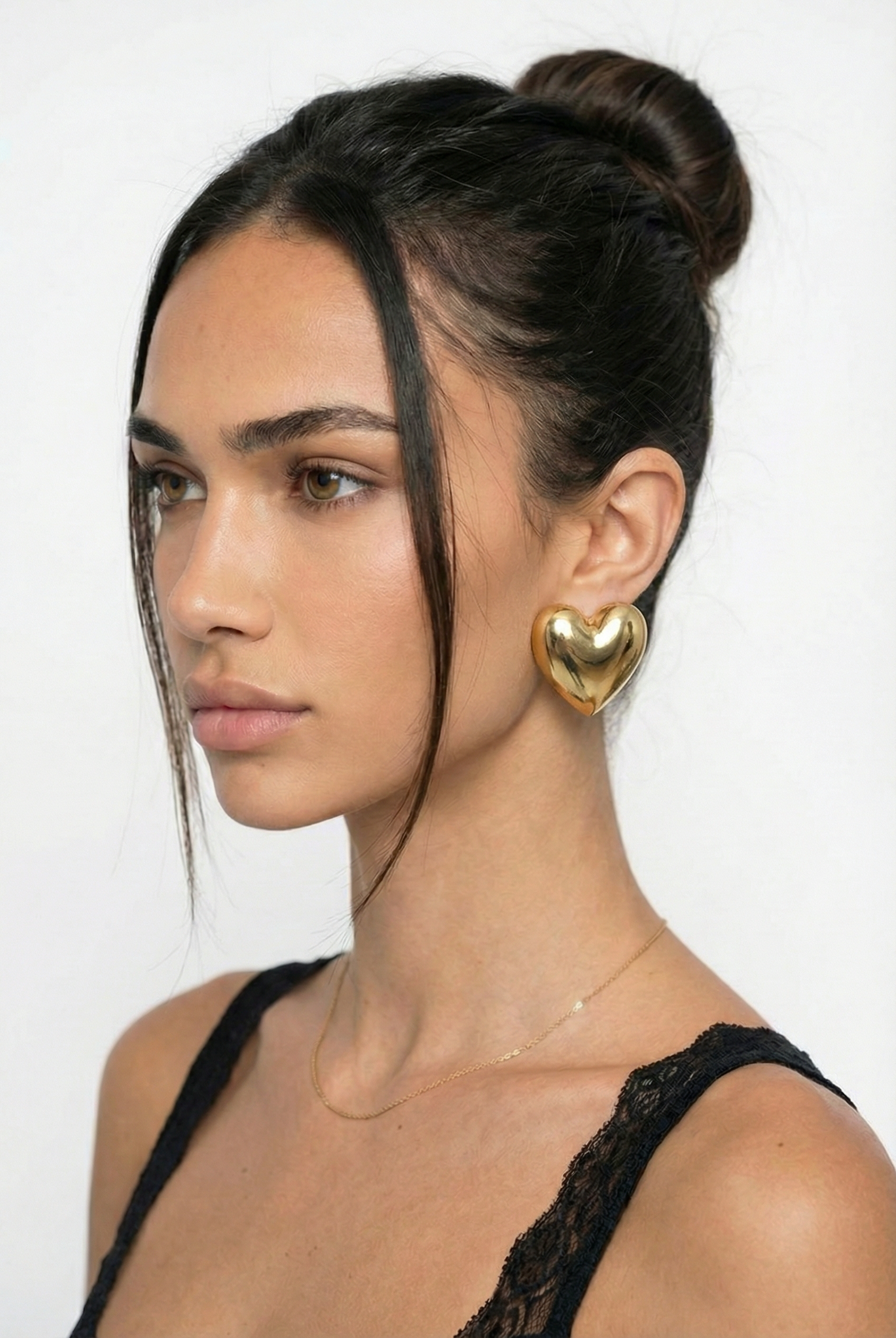 Woman with a stylish hair bun wearing gold heart-shaped earrings against a white background