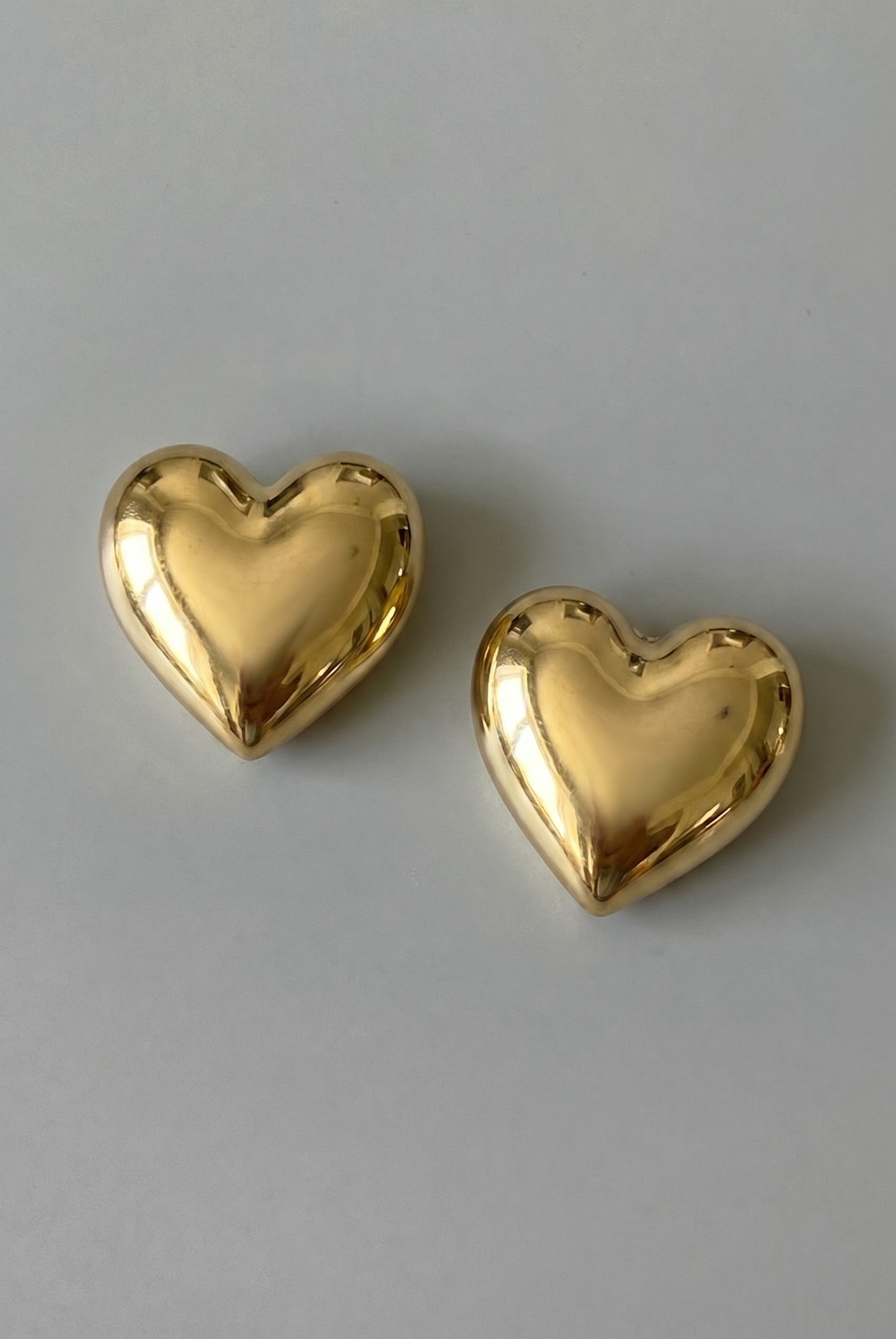 Two gold heart-shaped earrings on a gray background