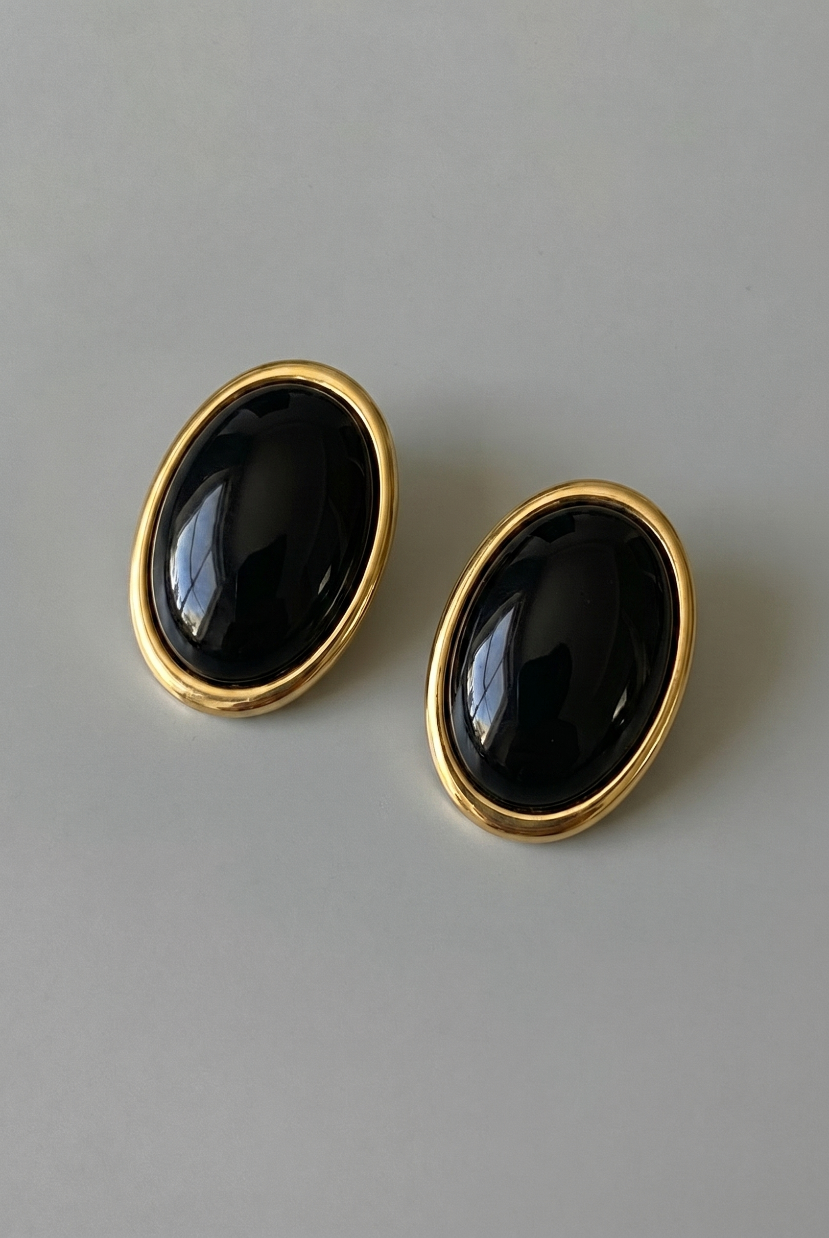 Pair of black oval earrings with gold rims on a gray background