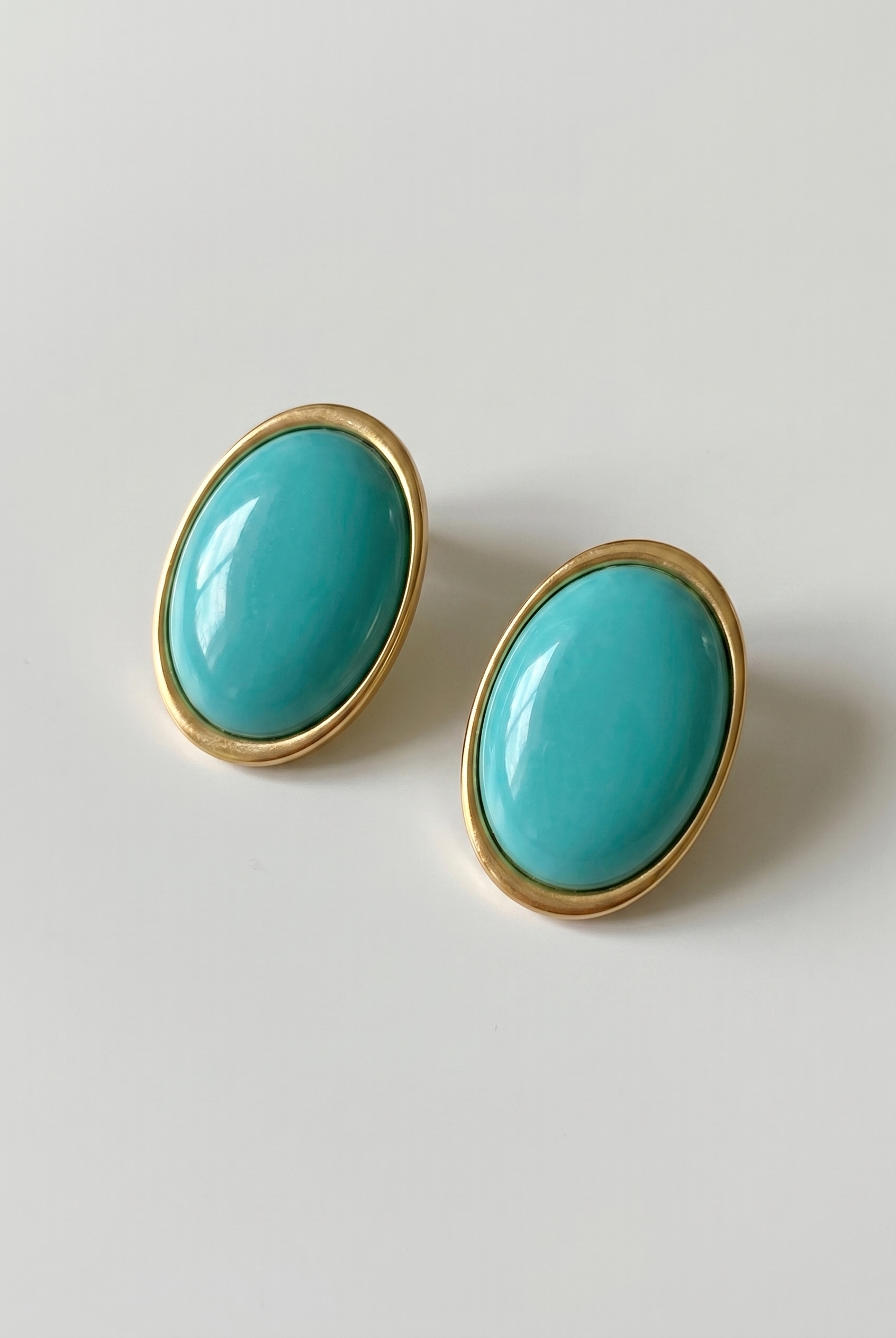 Turquoise earrings with gold frames on a light gray background