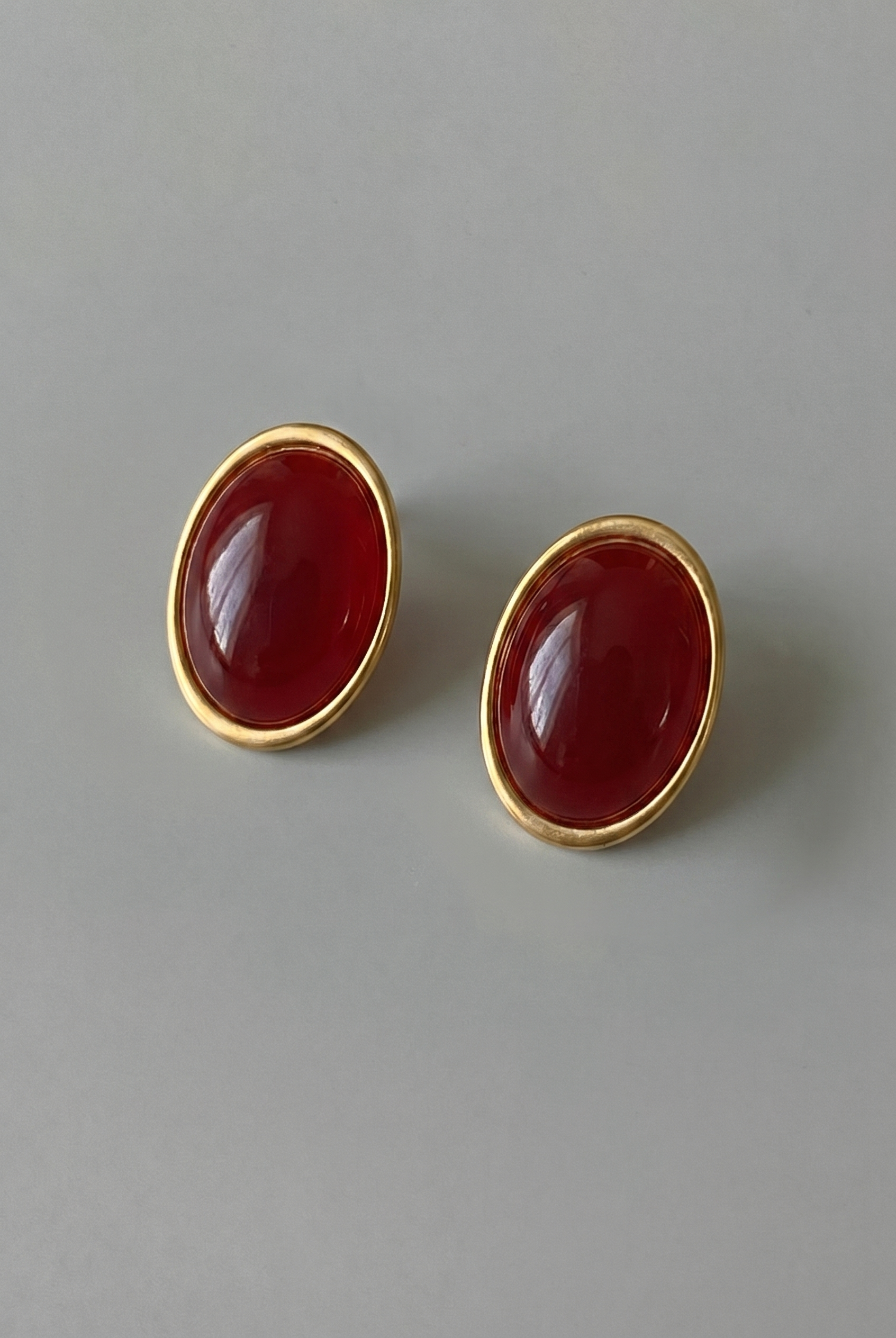 Pair of gold earrings with red stones on a gray background