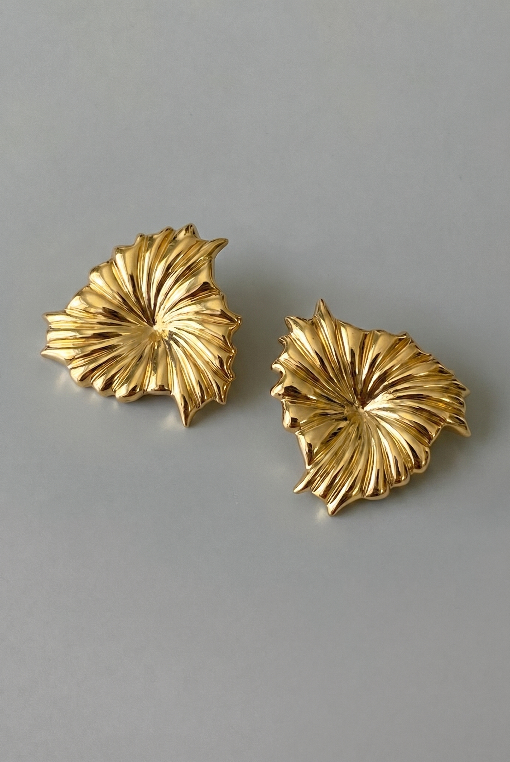 Pair of gold leaf-shaped earrings on a gray background