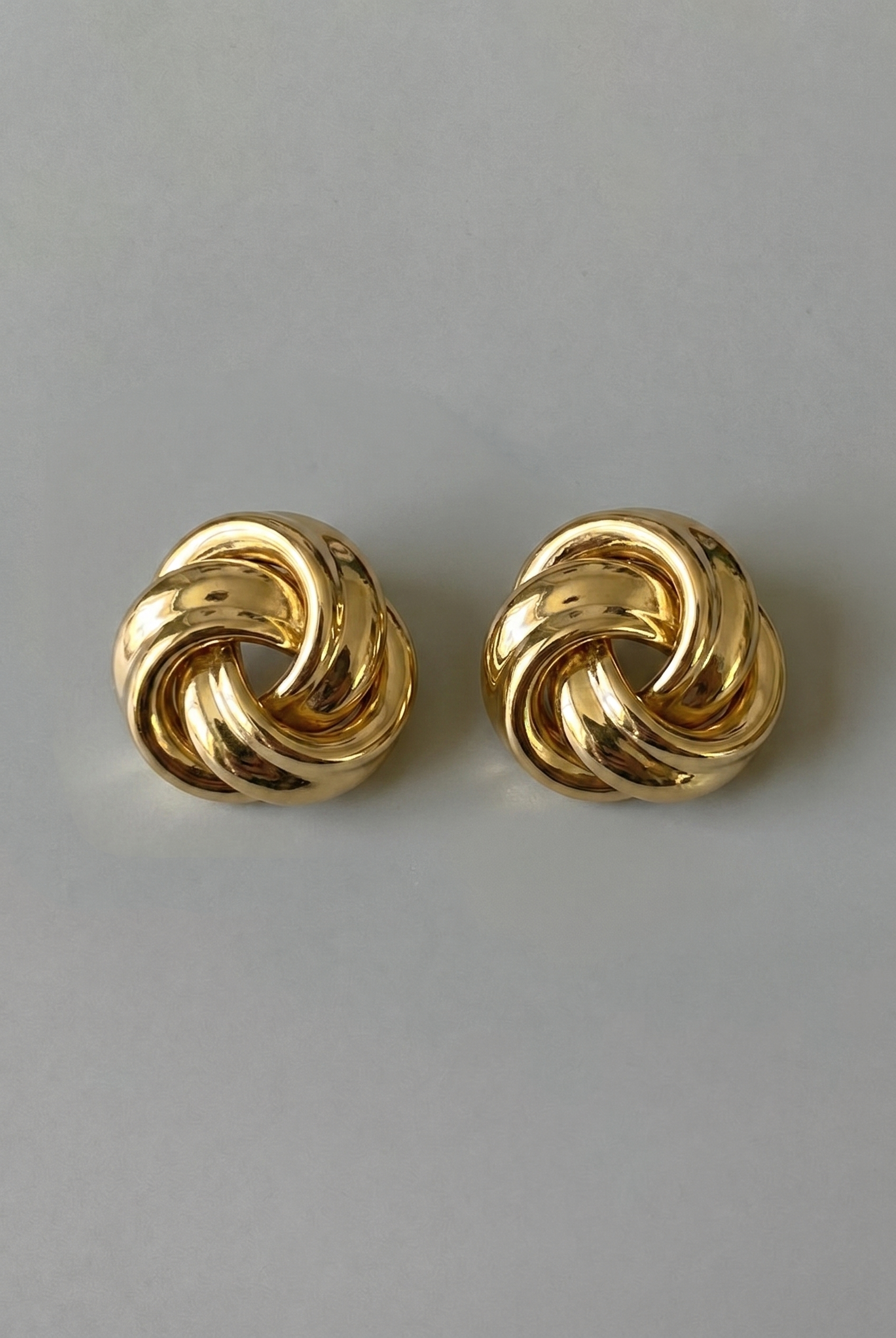 Pair of gold knot earrings on a gray background