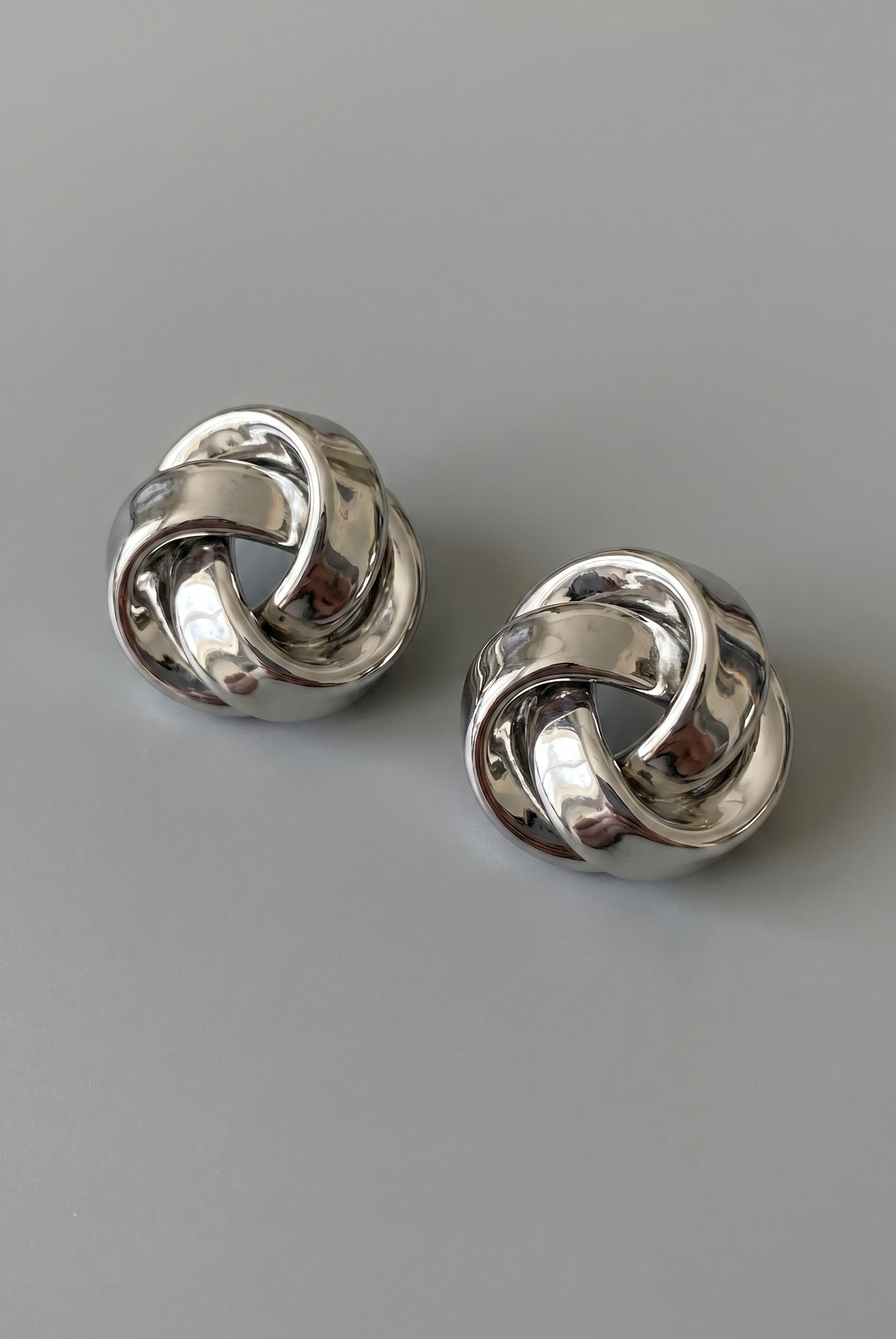 Pair of silver knot earrings on a gray background