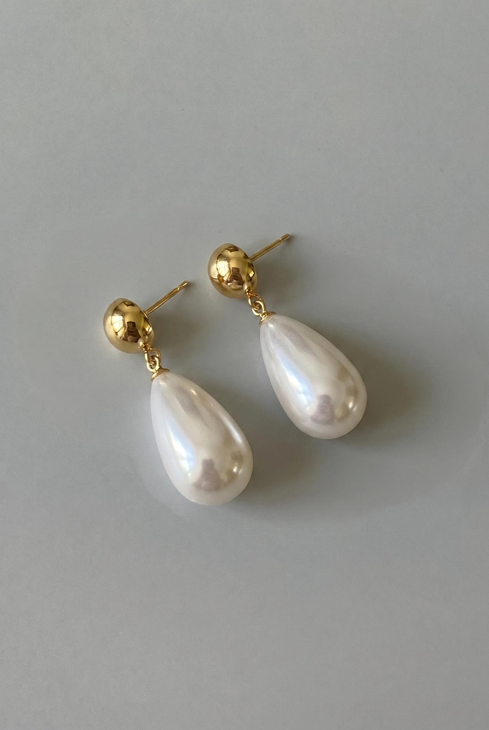 Pearl earrings with gold posts on a light gray background