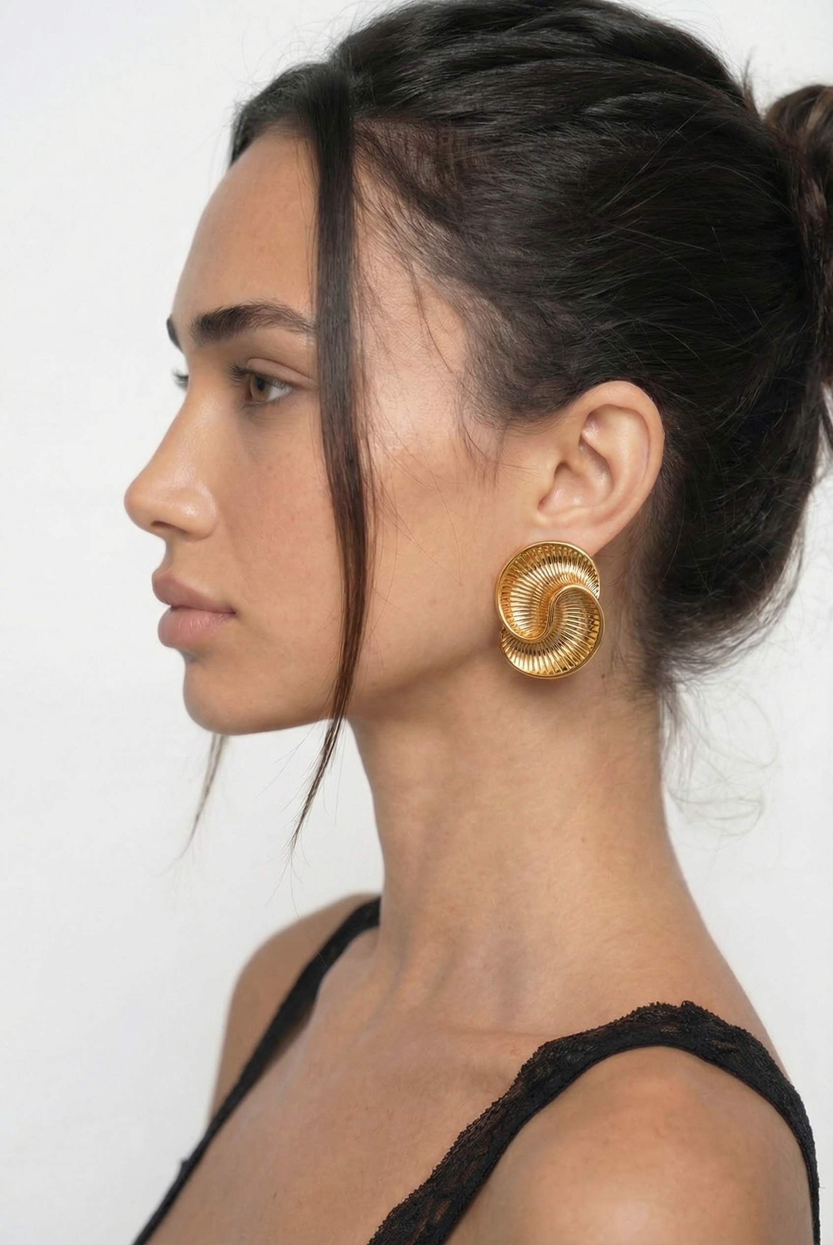 Woman wearing gold spiral earrings against a white background