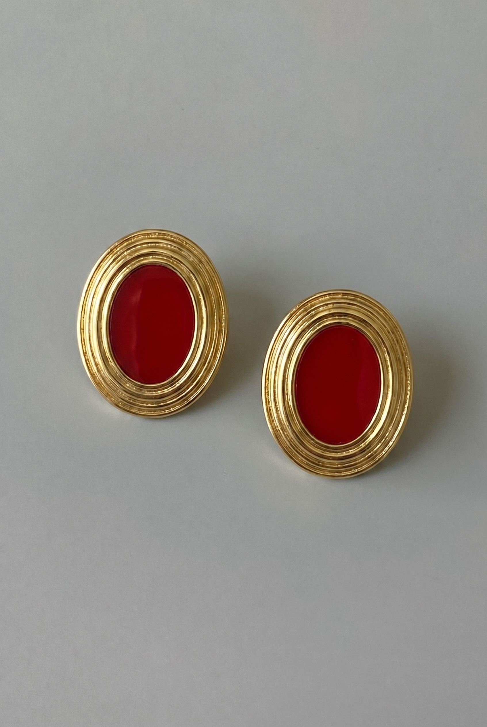 Pair of gold earrings with red stones on a gray background