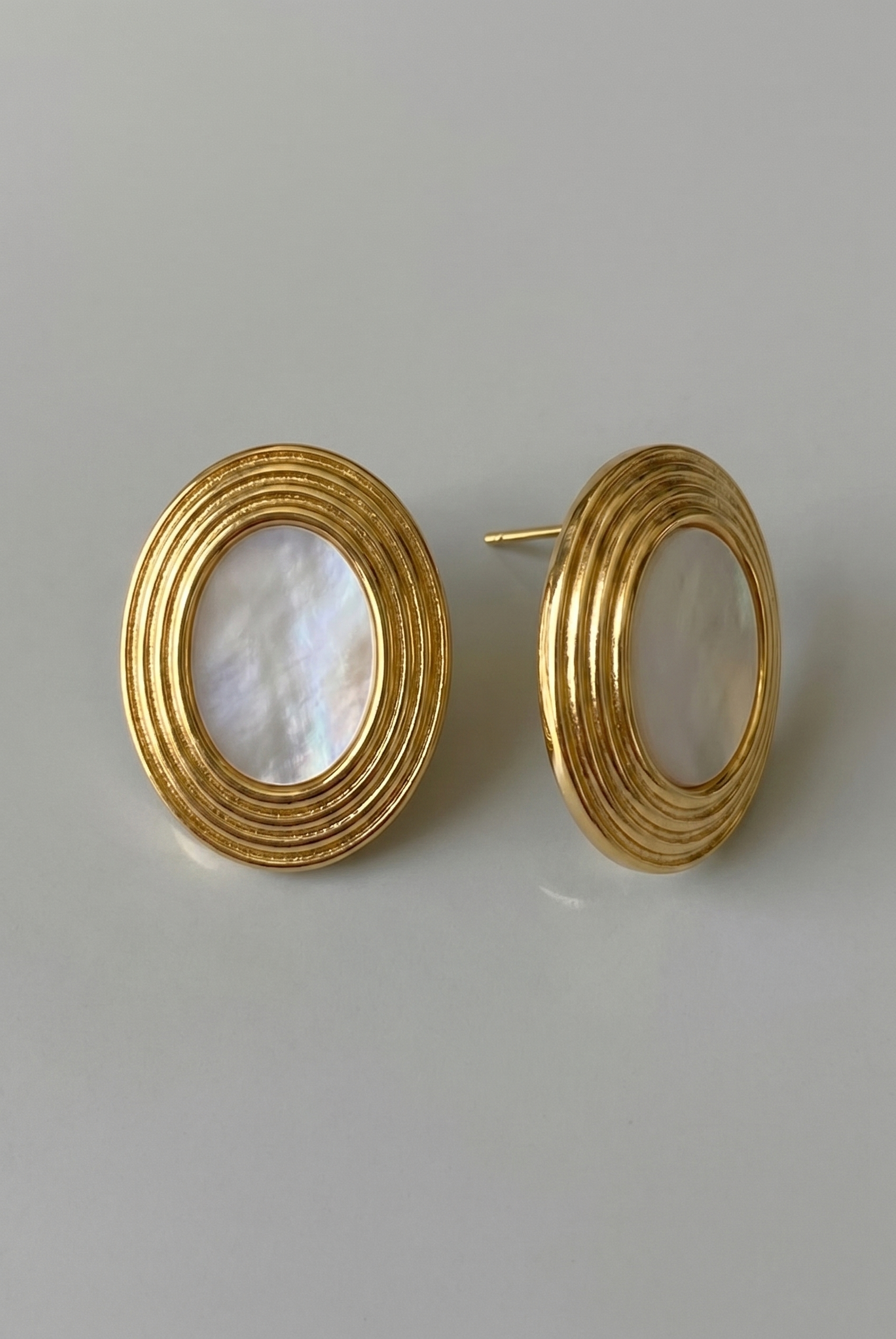Gold hoop earrings with a central pearl-like stone on a light gray background