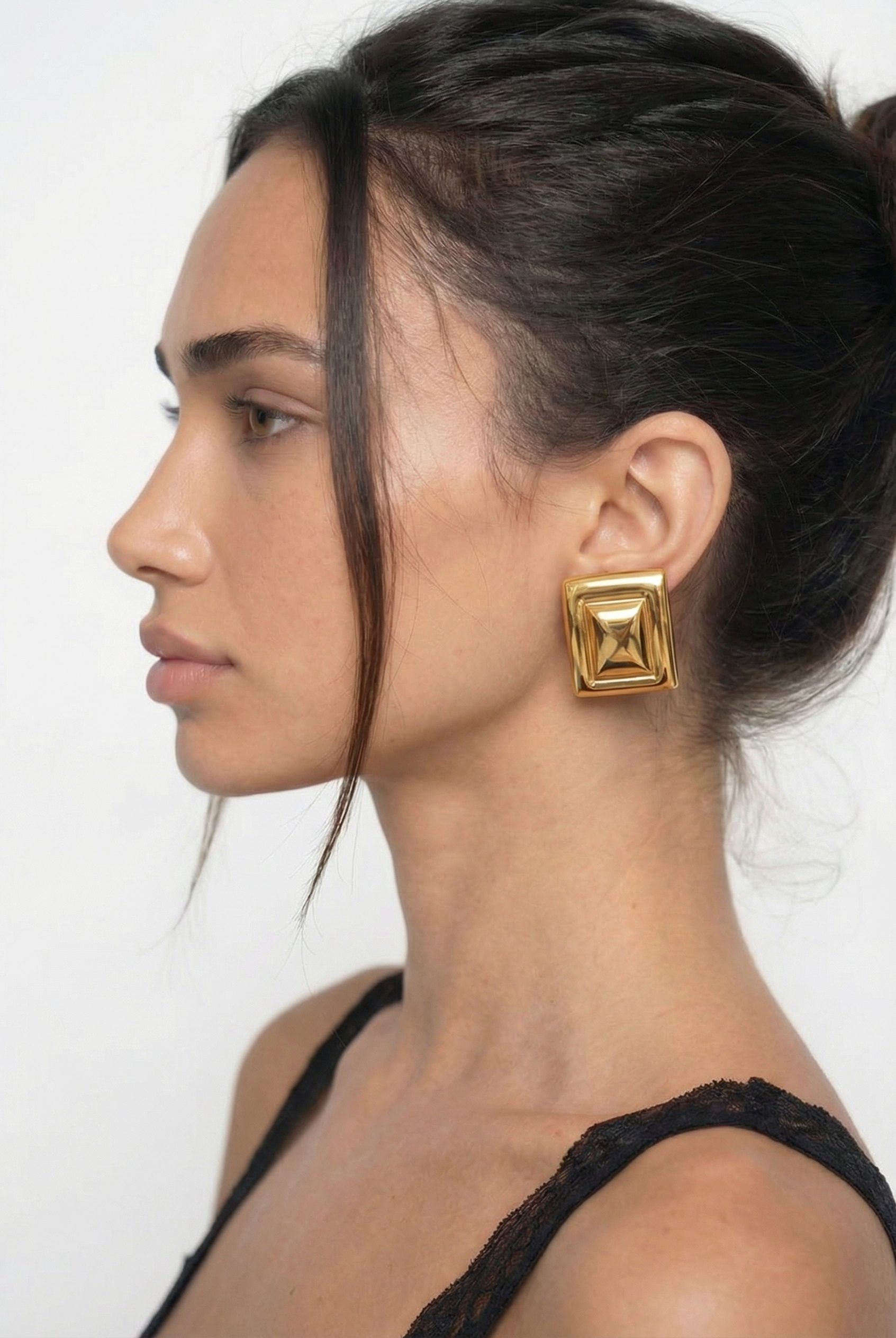 Woman wearing gold square earrings against a white background