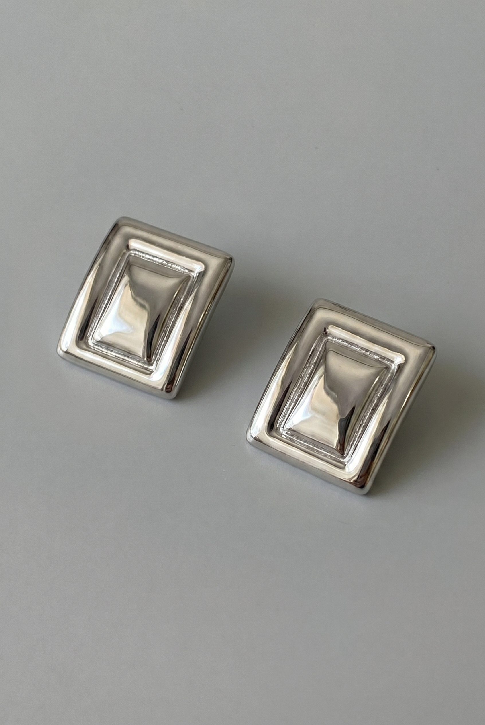 Pair of silver square earrings on a gray background
