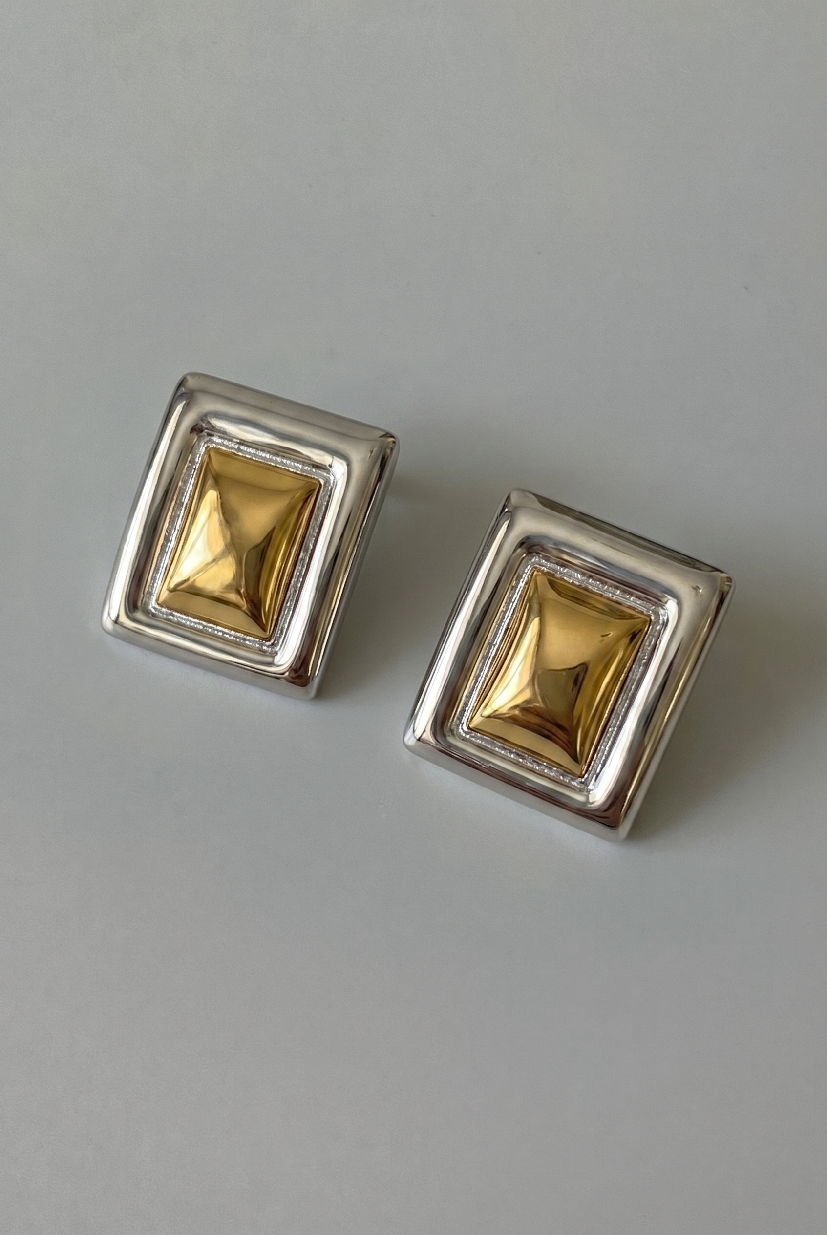Pair of square gold earrings with silver frames on a gray background