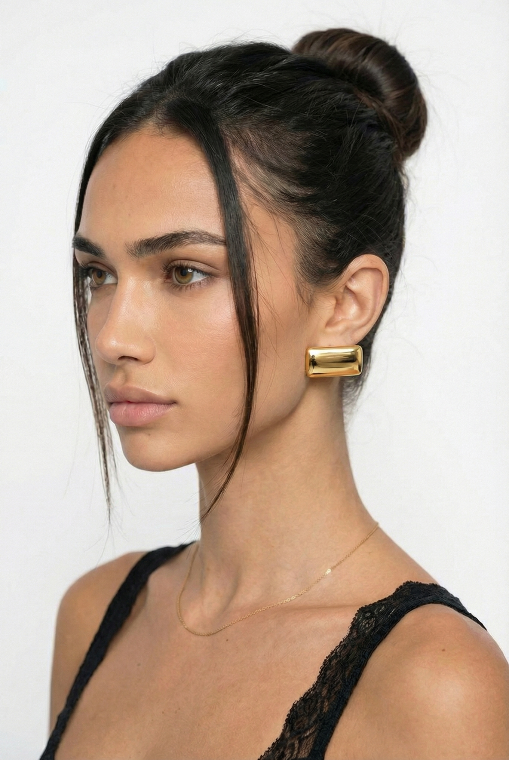 Woman with a stylish hair bun and gold earring on a white background