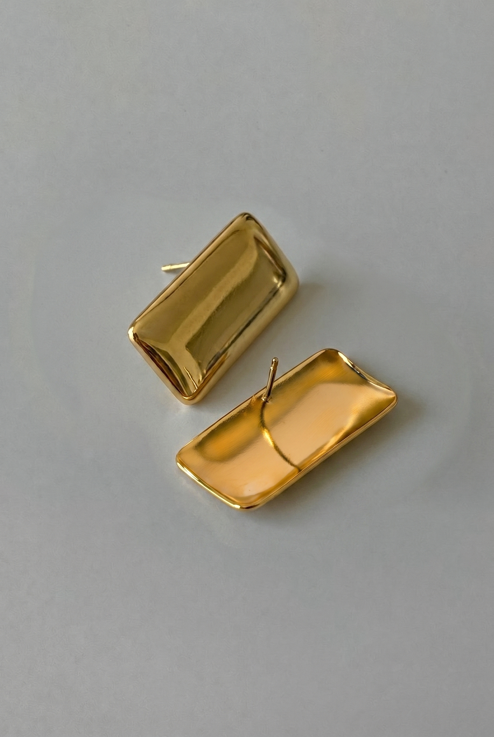 Gold rectangular earrings on a gray background