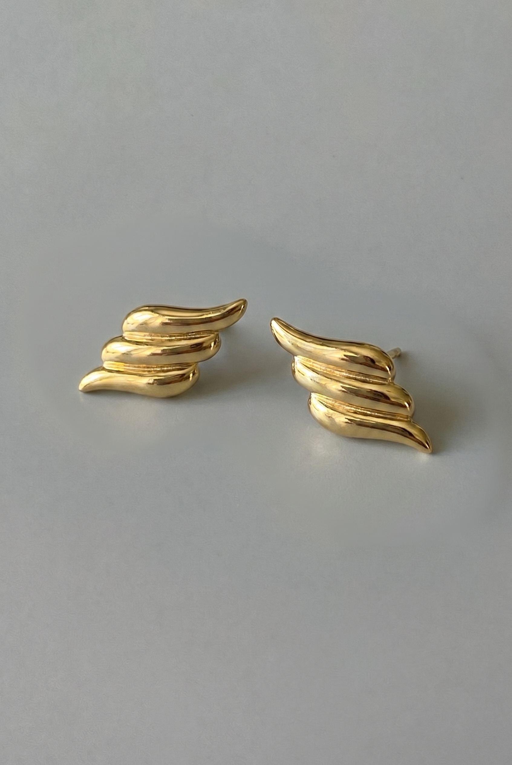 Gold wing-shaped earrings on a gray background