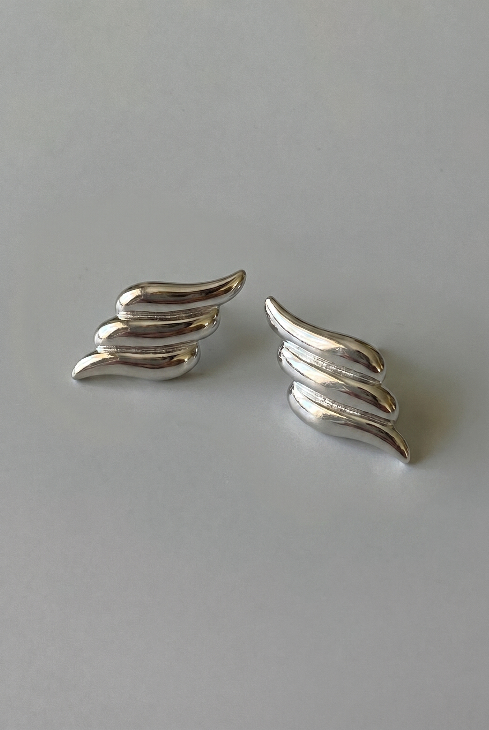 Pair of silver wing-shaped earrings on a gray background