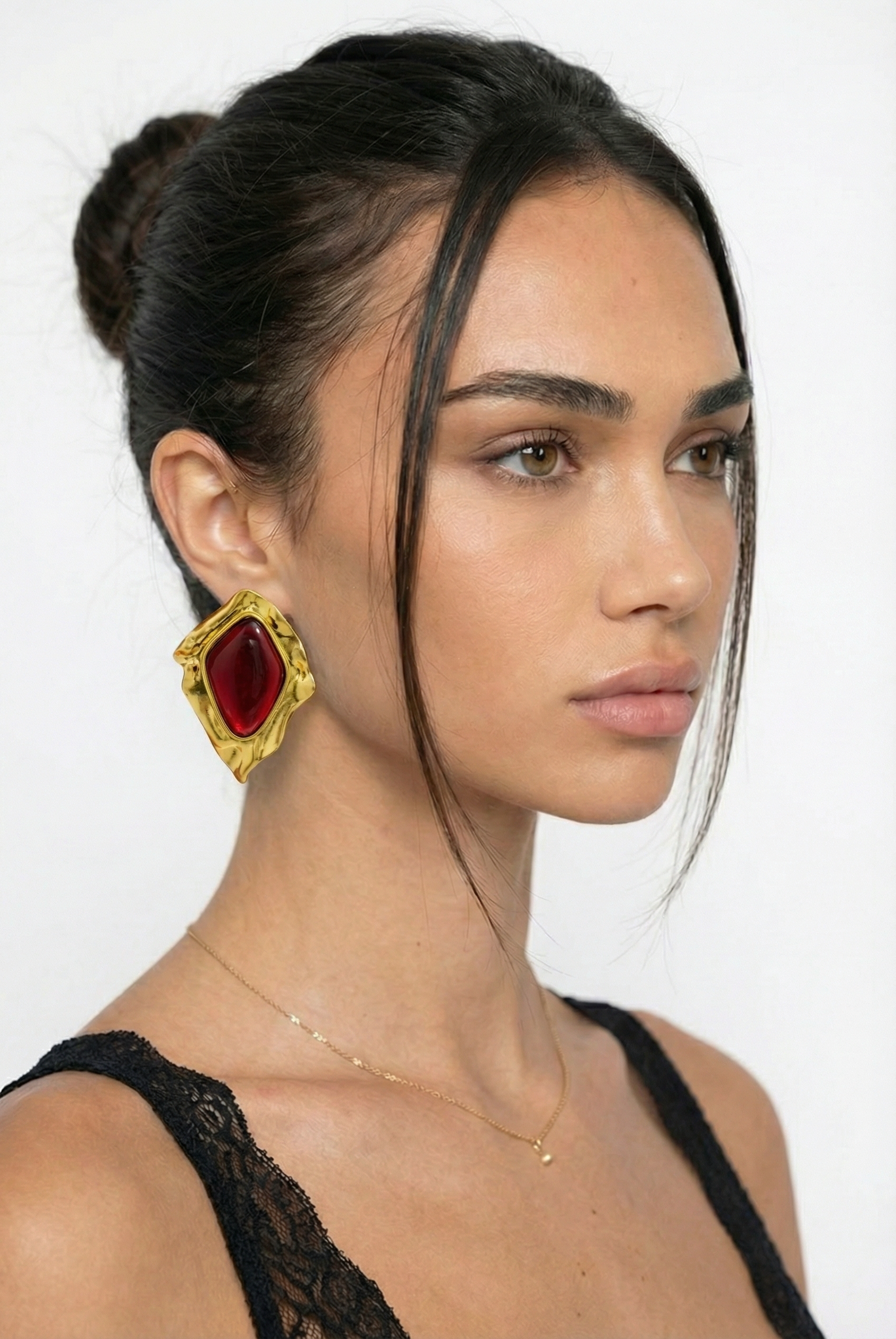 Woman wearing gold earrings with a red gemstone on a white background