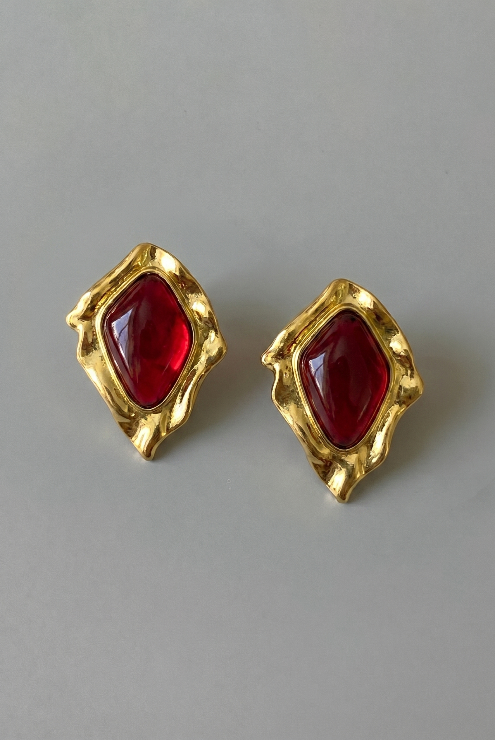 Gold earrings with red gemstones on a gray background