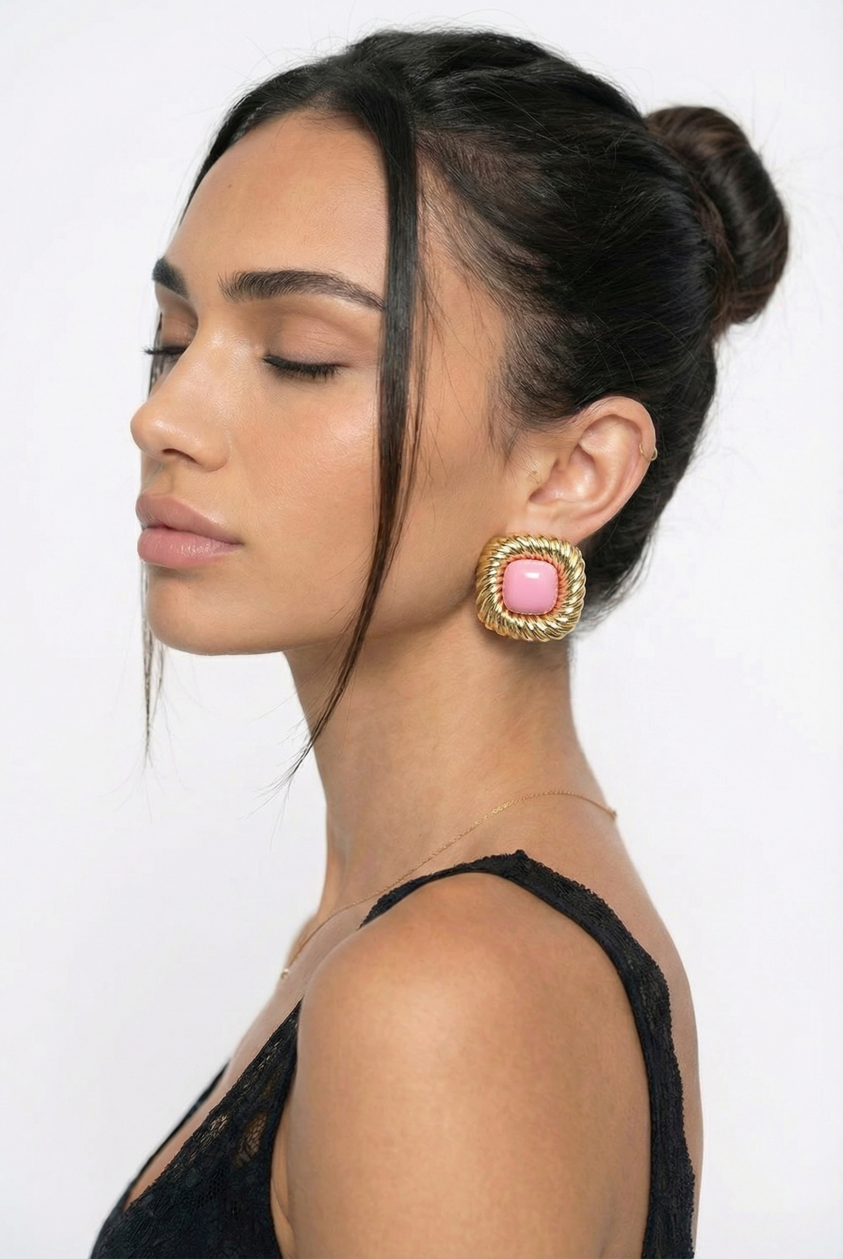 Woman wearing large earrings with a pink gemstone on a plain background