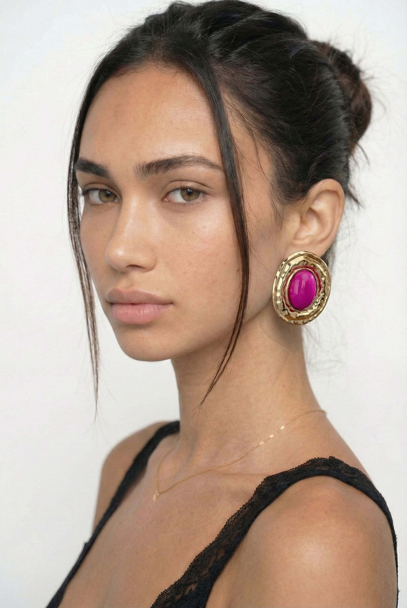 Woman wearing a large gold earring with a pink gemstone on a white background