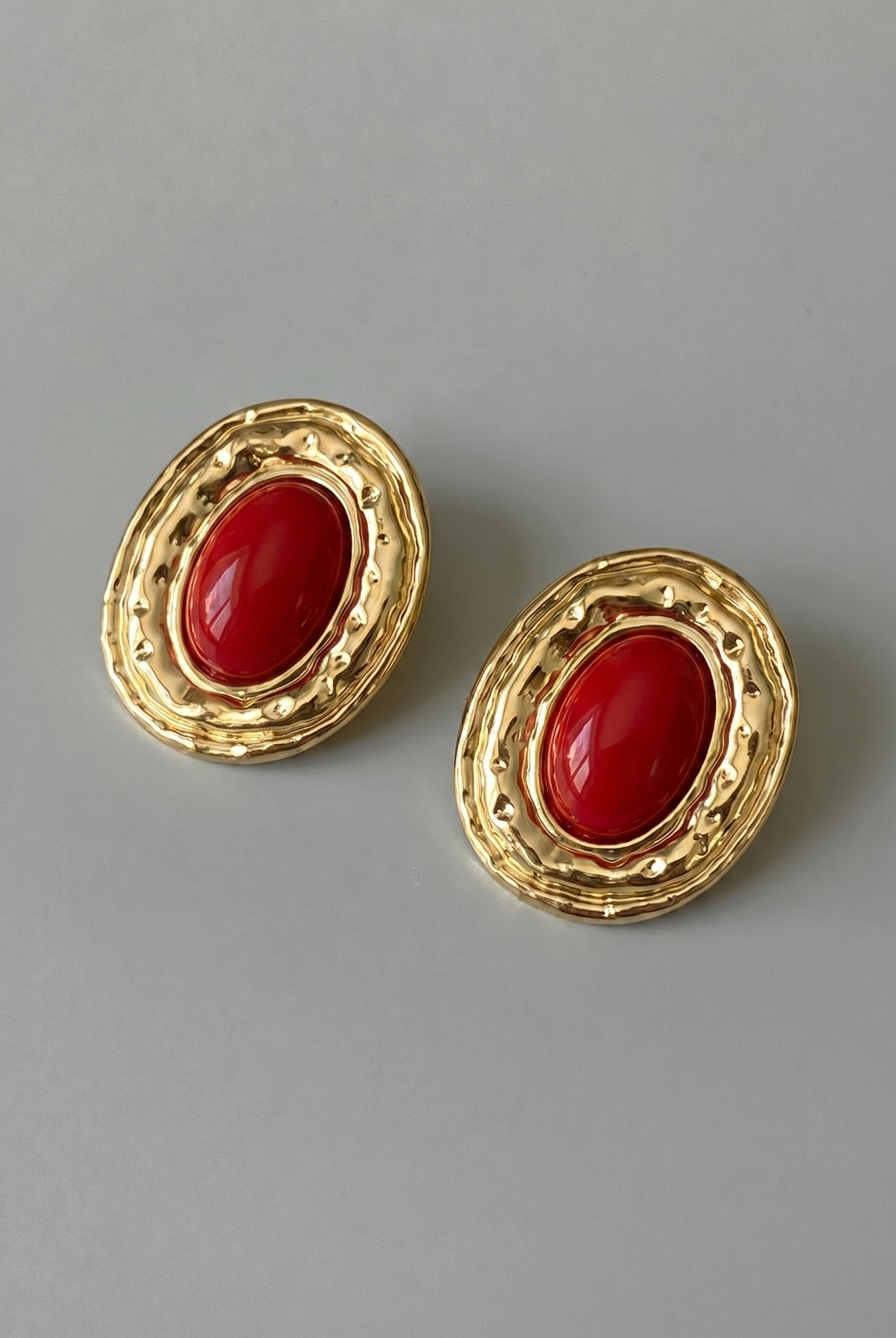 Pair of gold earrings with red stones on a gray background