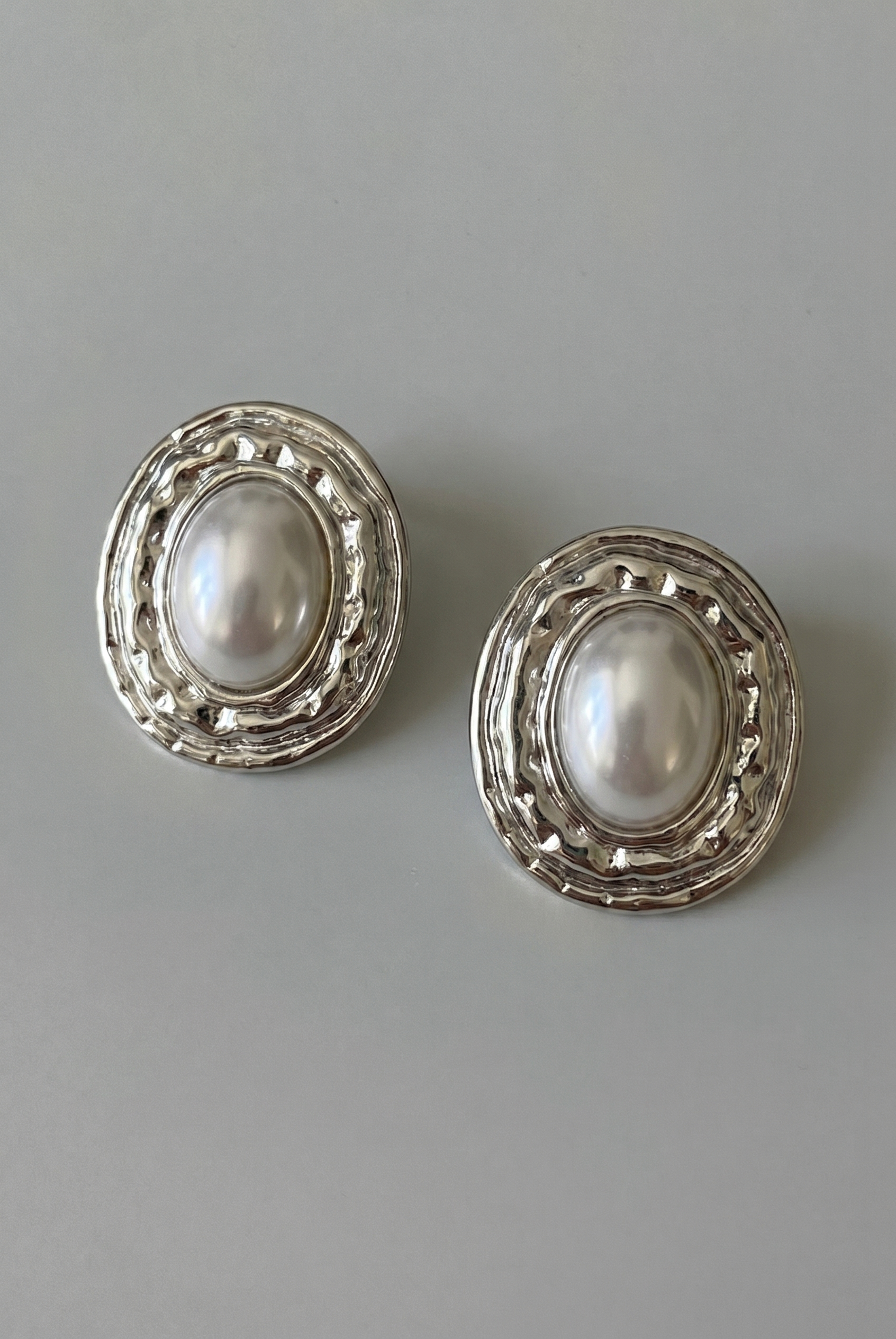 Pair of pearl earrings with silver decorative frames on a gray background