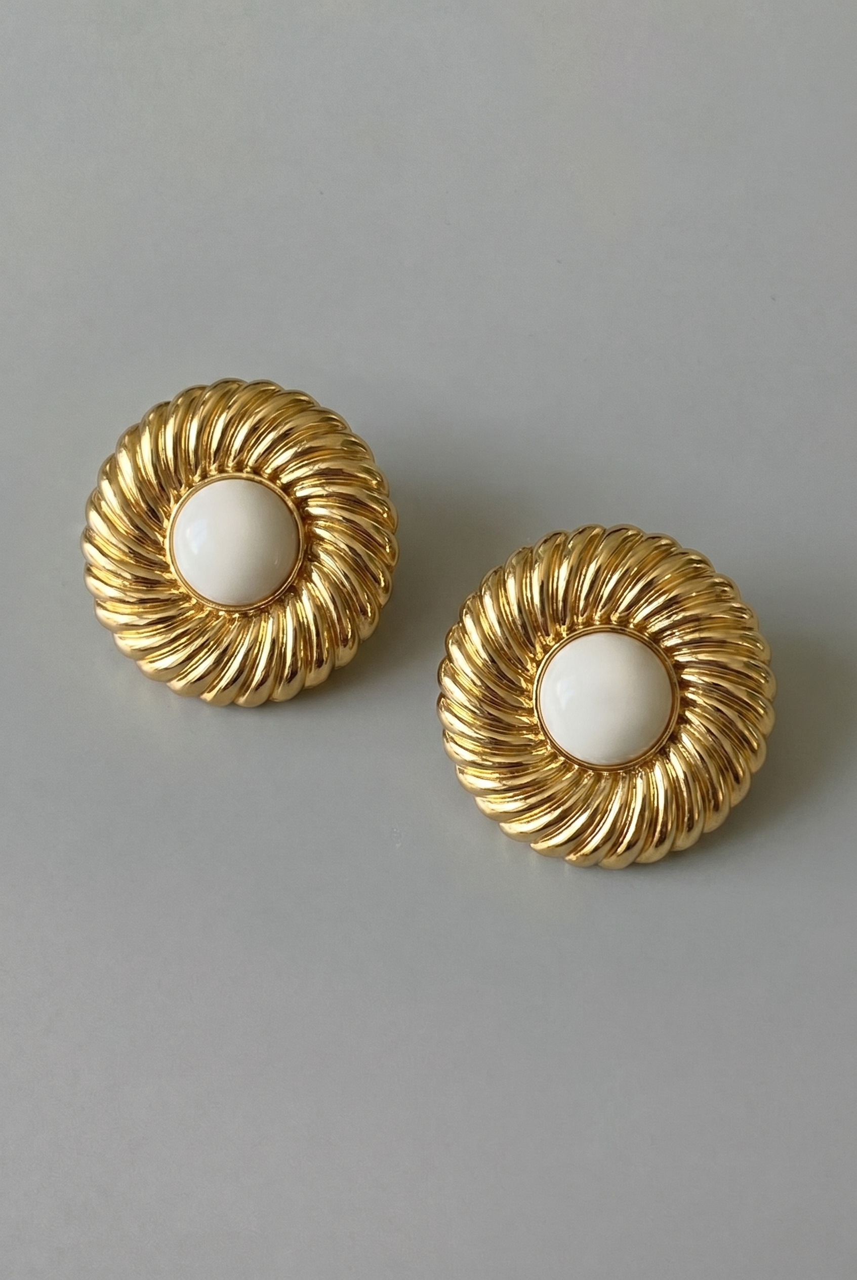 Pair of gold earrings with white centers on a gray background