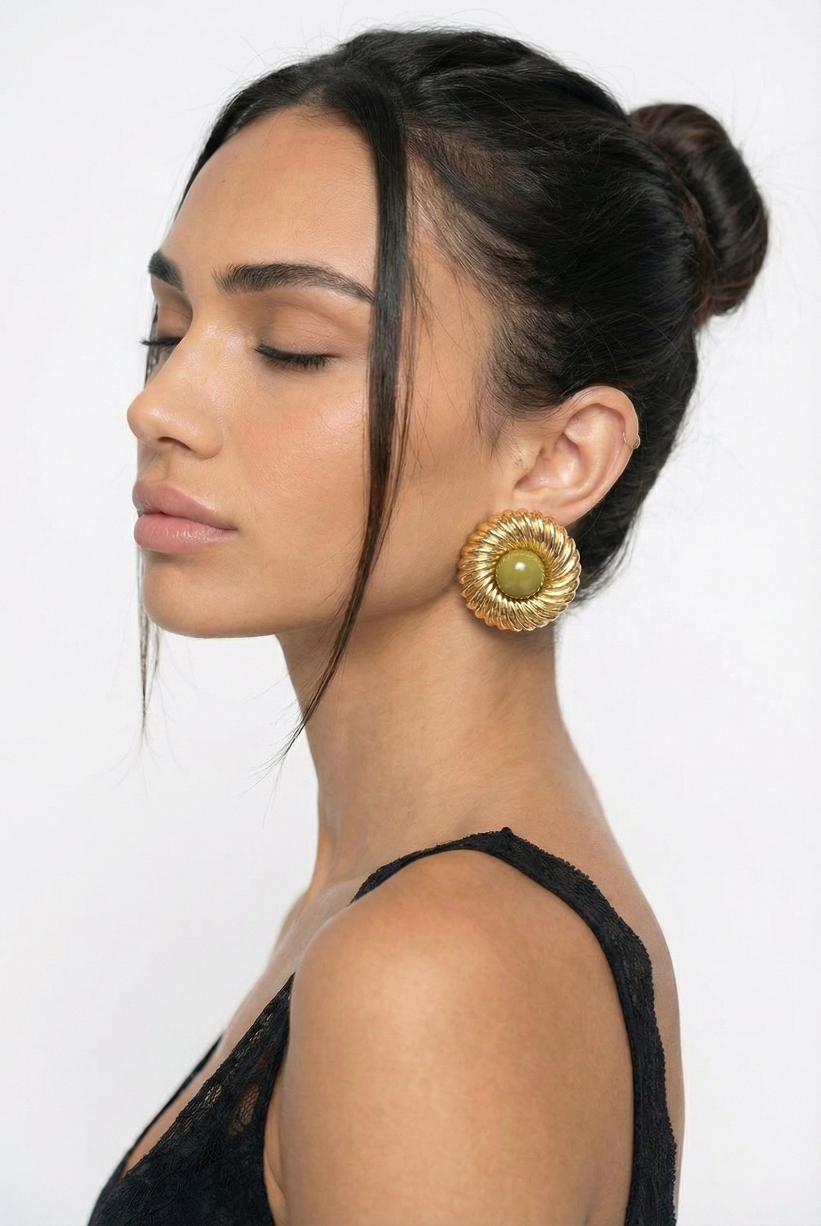 Woman wearing a large gold earring with a green gemstone on a white background