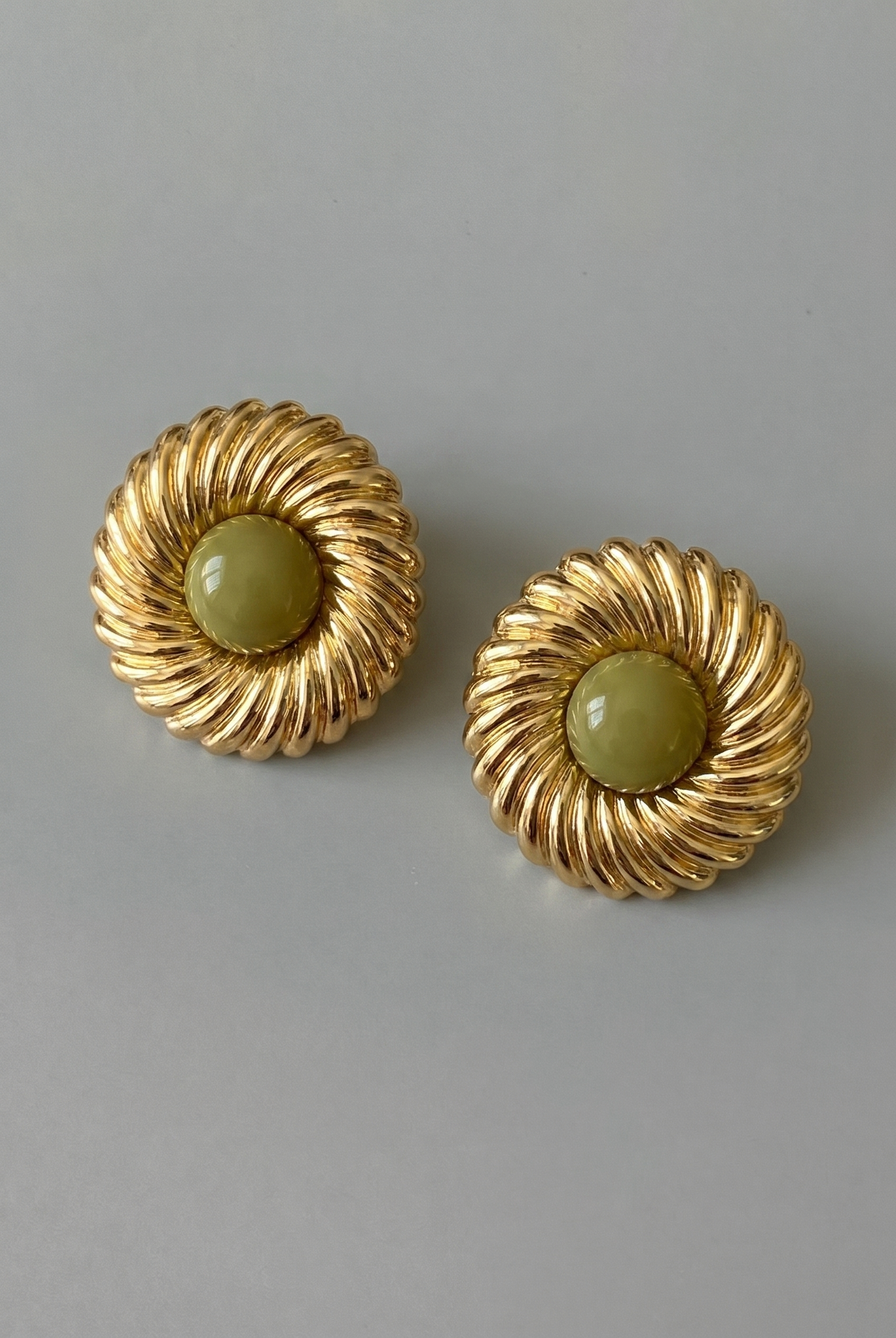 Pair of gold earrings with green stones on a gray background