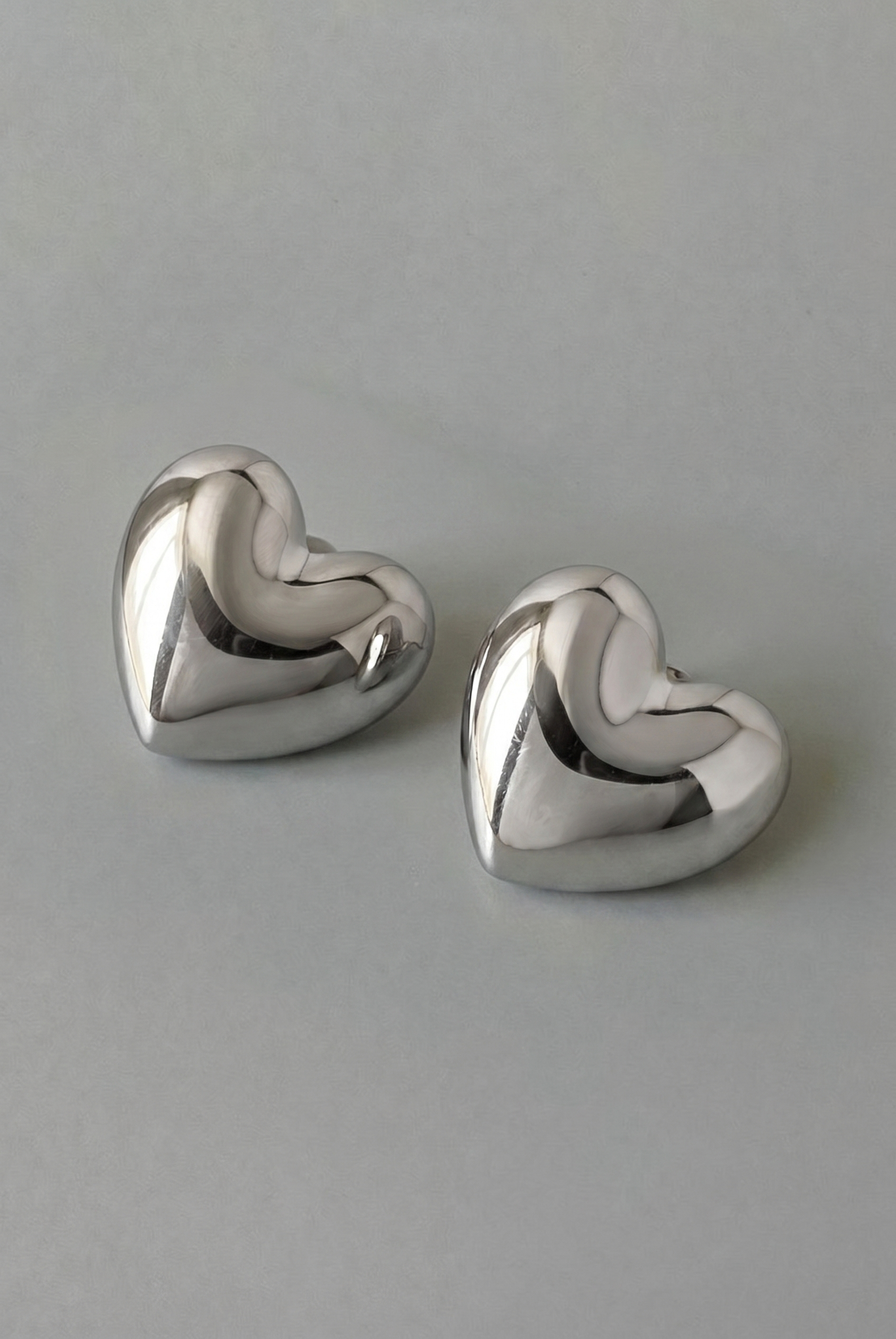 Pair of silver heart-shaped earrings on a gray background