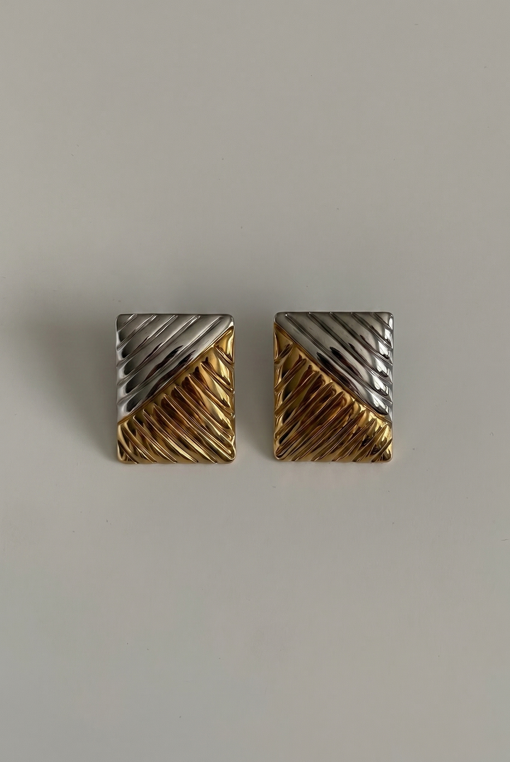 Pair of gold and silver geometric earrings on a light gray background