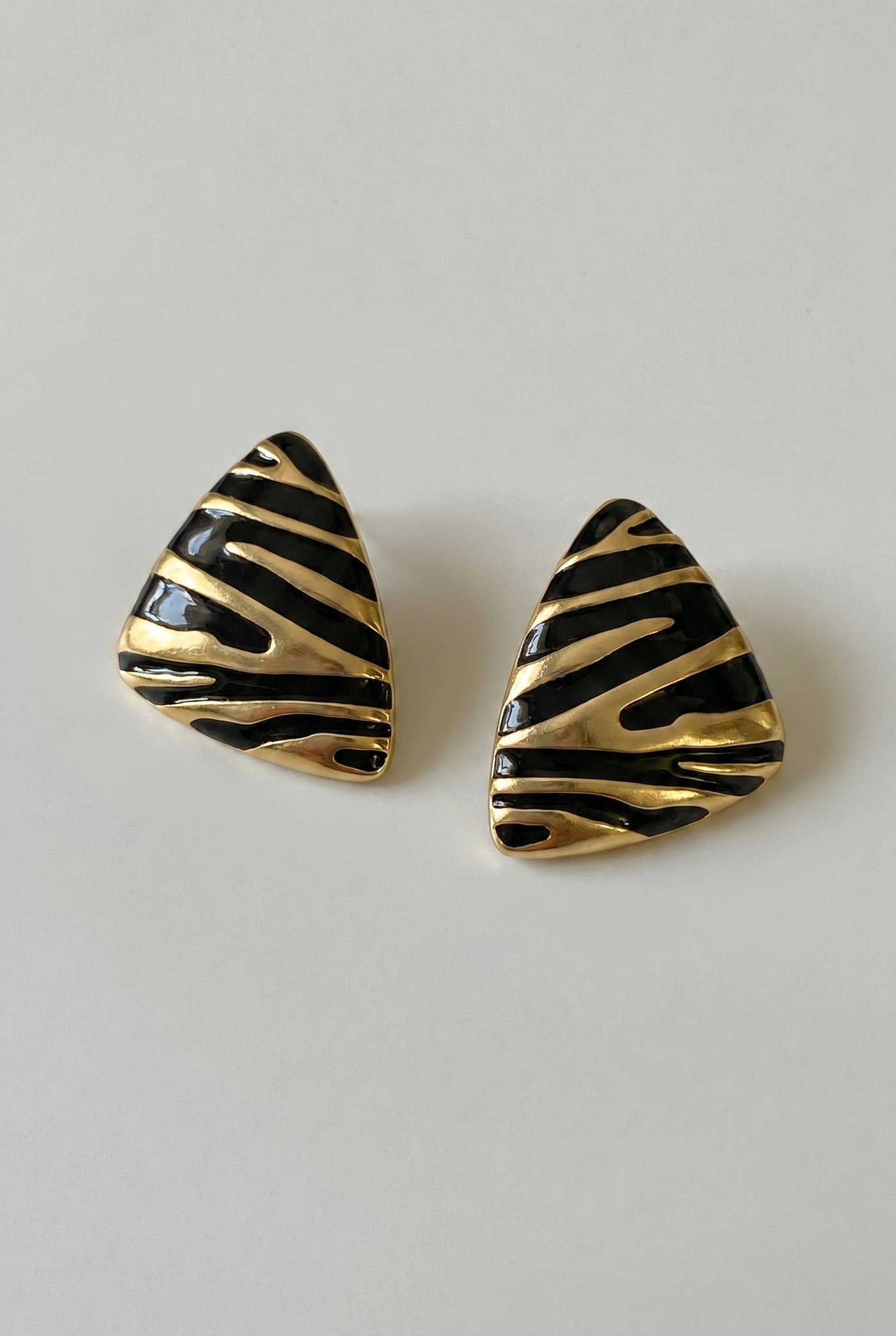 Pair of gold and black striped earrings on a light gray background
