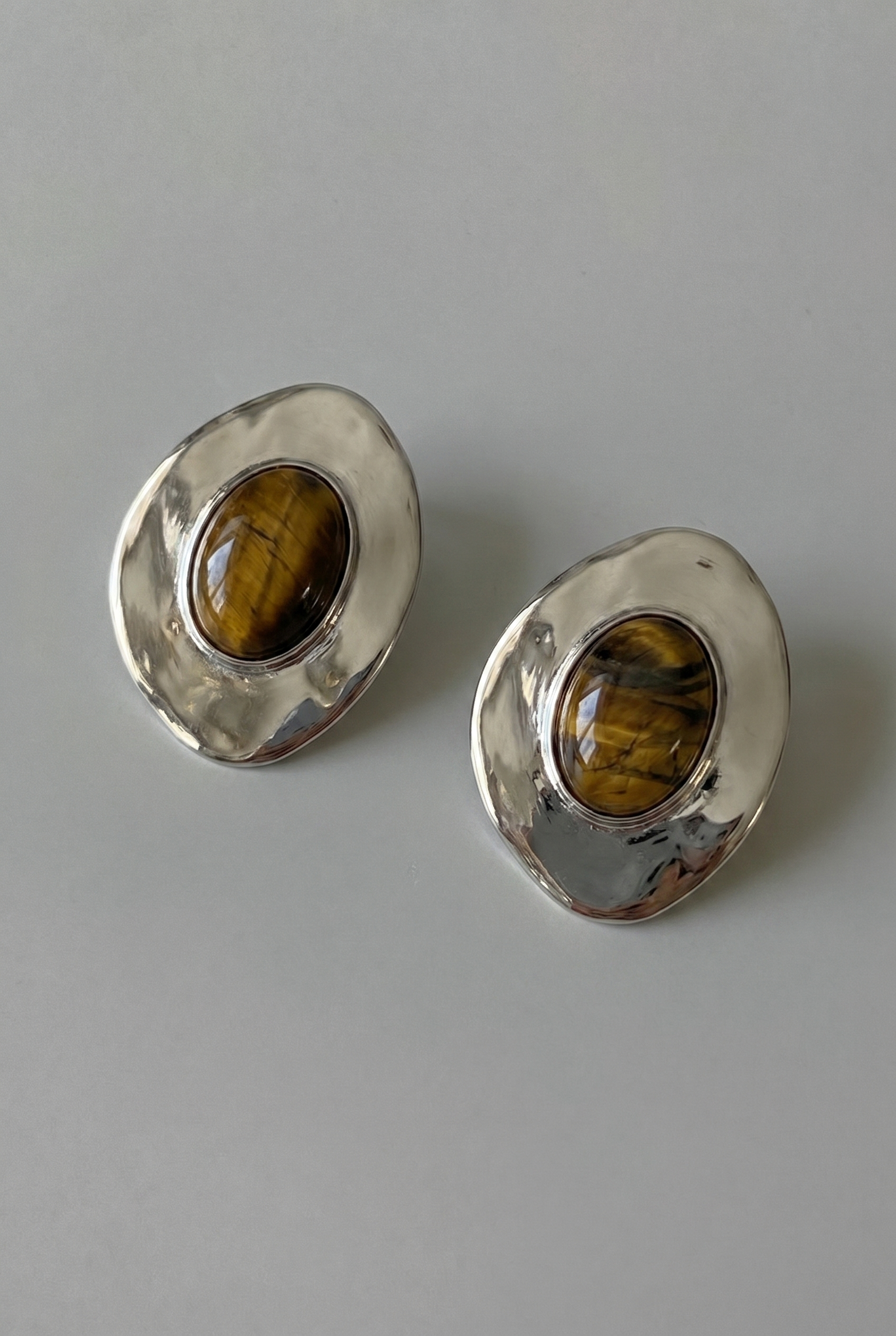 Pair of silver earrings with tiger's eye stones on a gray background