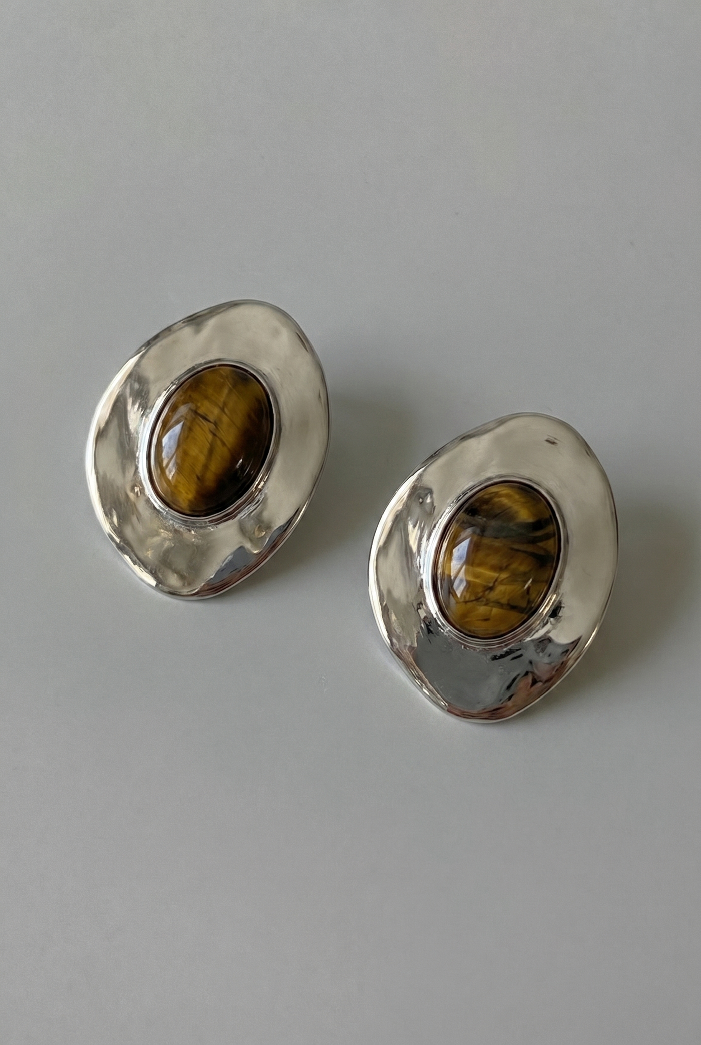 Pair of silver earrings with tiger's eye stones on a gray background