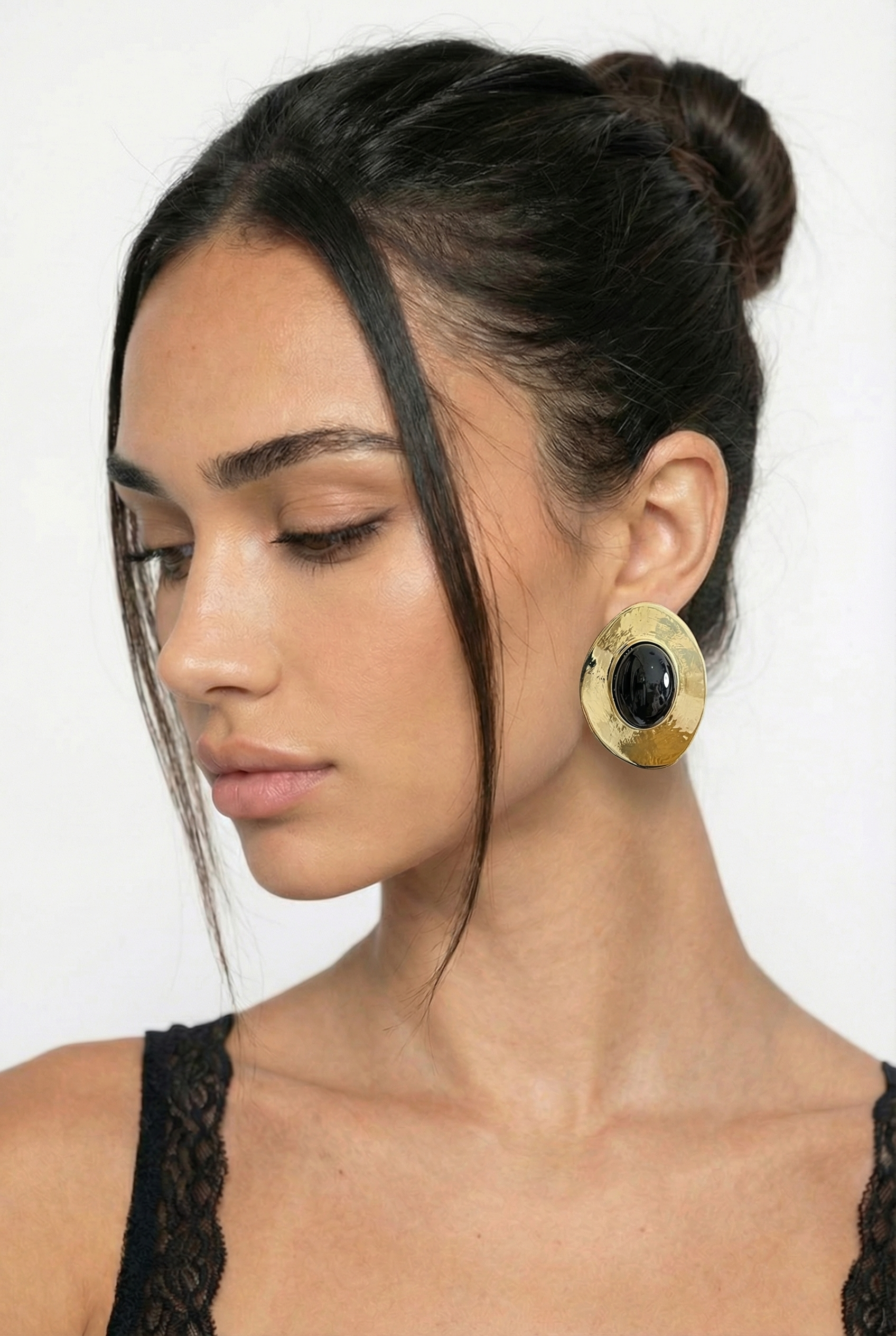 Woman wearing gold earrings with a black stone on a white background
