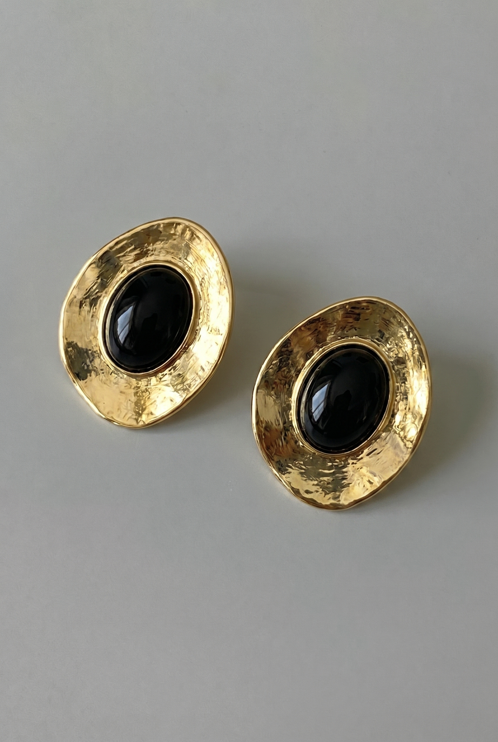 Pair of gold earrings with black stones on a gray background