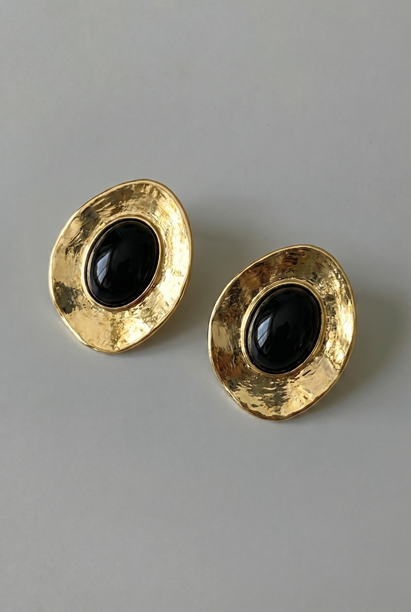 Pair of gold earrings with black stones on a gray background