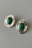 Pair of silver earrings with green gemstones on a gray background