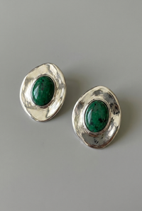Pair of silver earrings with green gemstones on a gray background