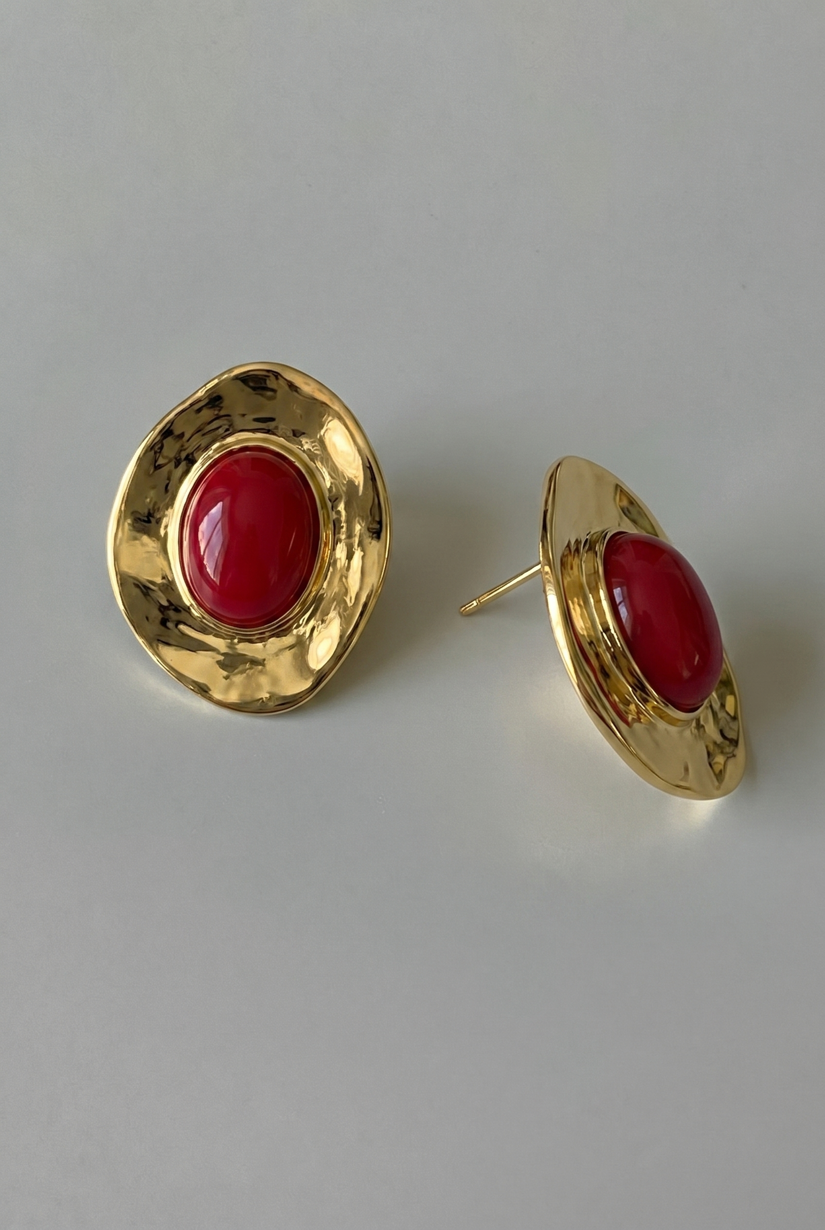 Gold earrings with red stones on a light gray background