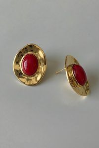 Gold earrings with red stones on a light gray background