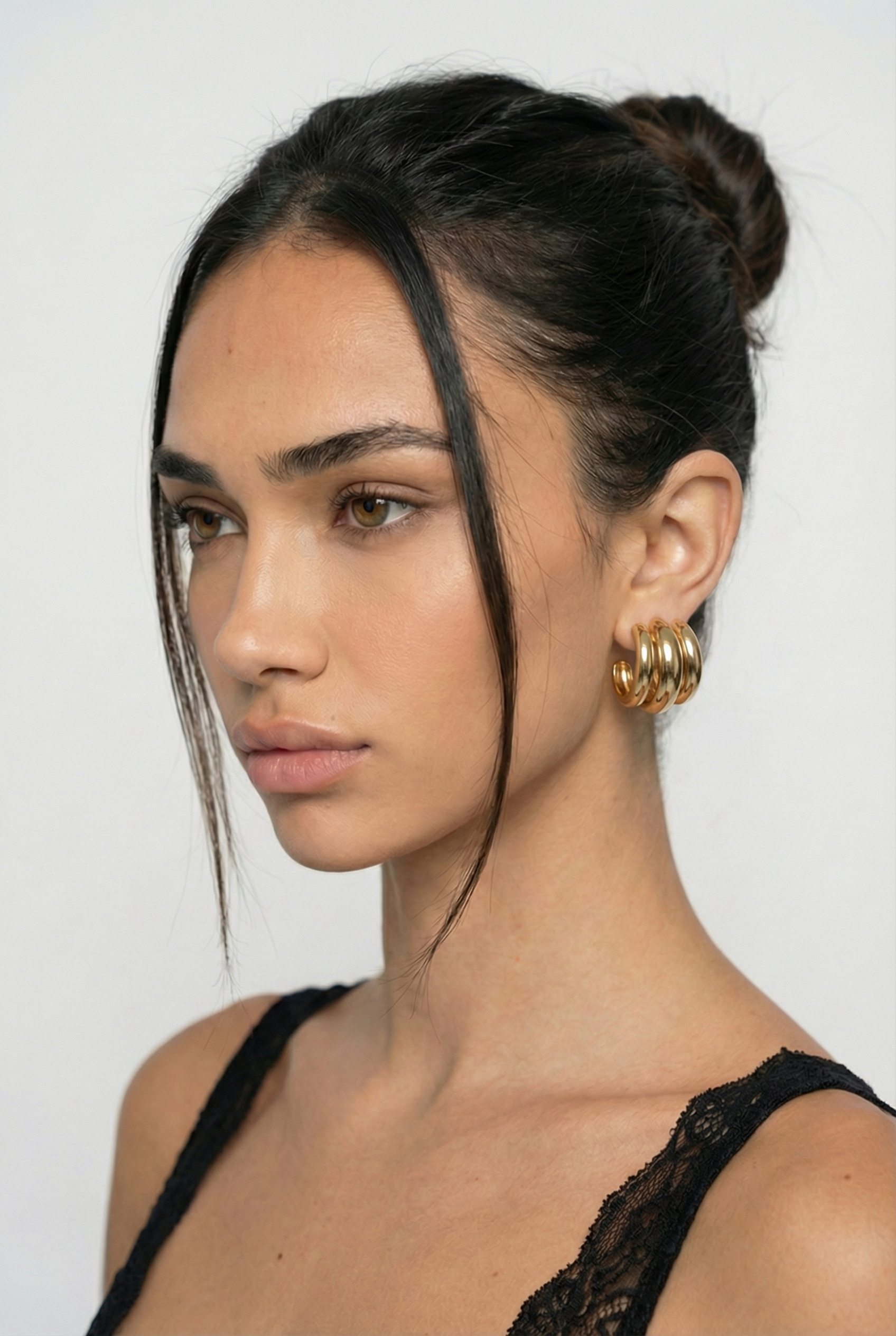 Woman with styled hair and gold earrings against a white background